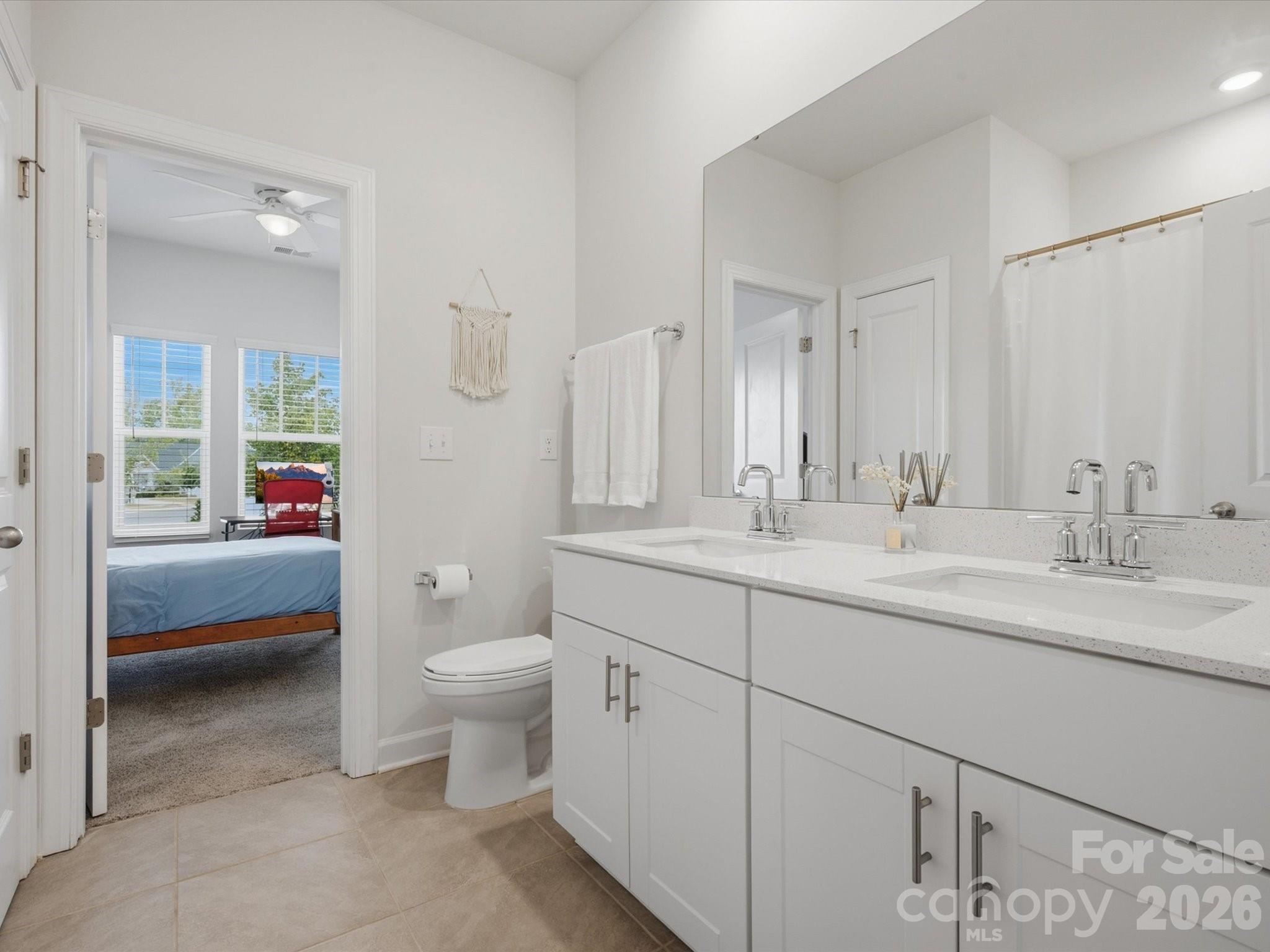 Bathroom with a long white double vanity and an open doorway to a bedroom.