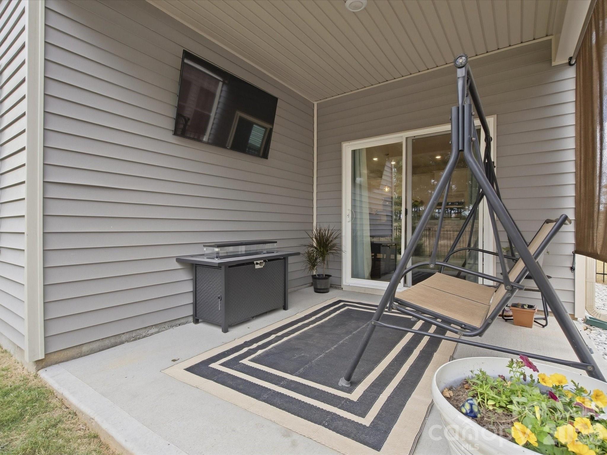 Covered patio with a hanging swing, wall-mounted television, and colorful flower planter.
