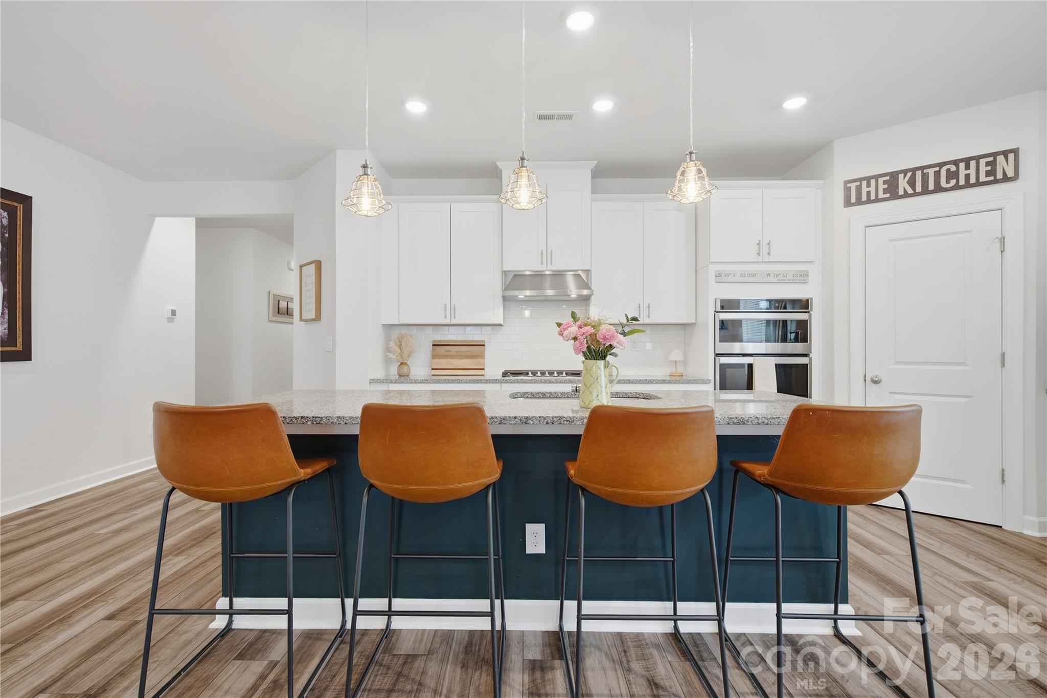 Bright kitchen with white cabinets, a dark blue island, and four brown bar stools.