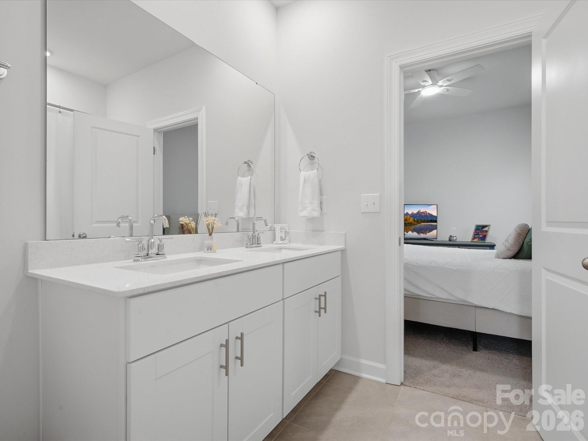 Bathroom with a white double vanity and large mirror, opening to a bedroom.
