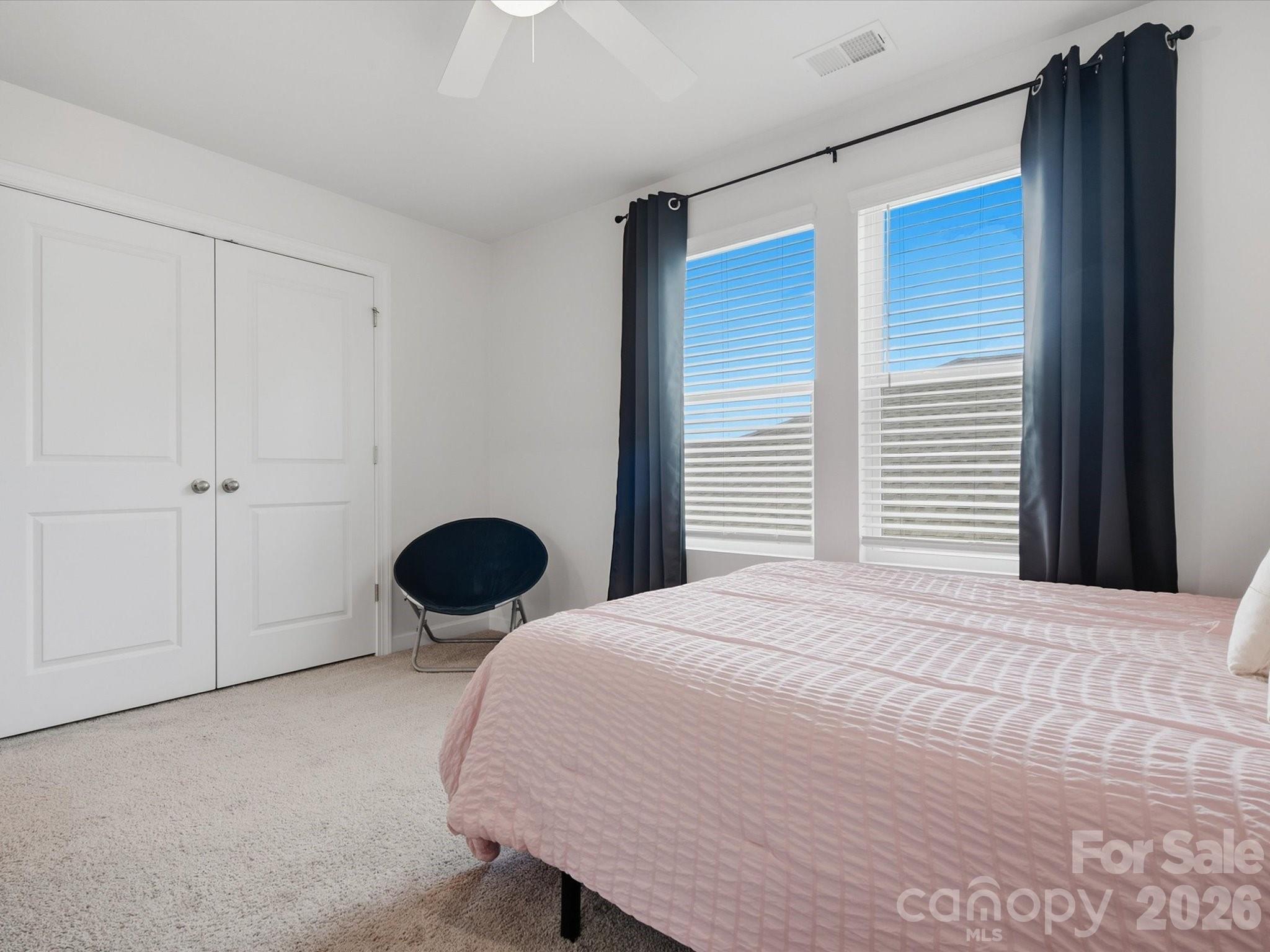 Bedroom with pale pink bedding, navy curtains, two bright windows, and white double closet doors.