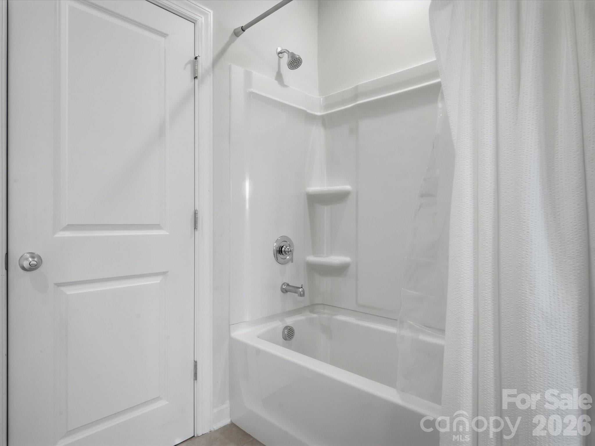 Bathroom with a white tub and shower, molded shelving, chrome fixtures, and a white curtain.