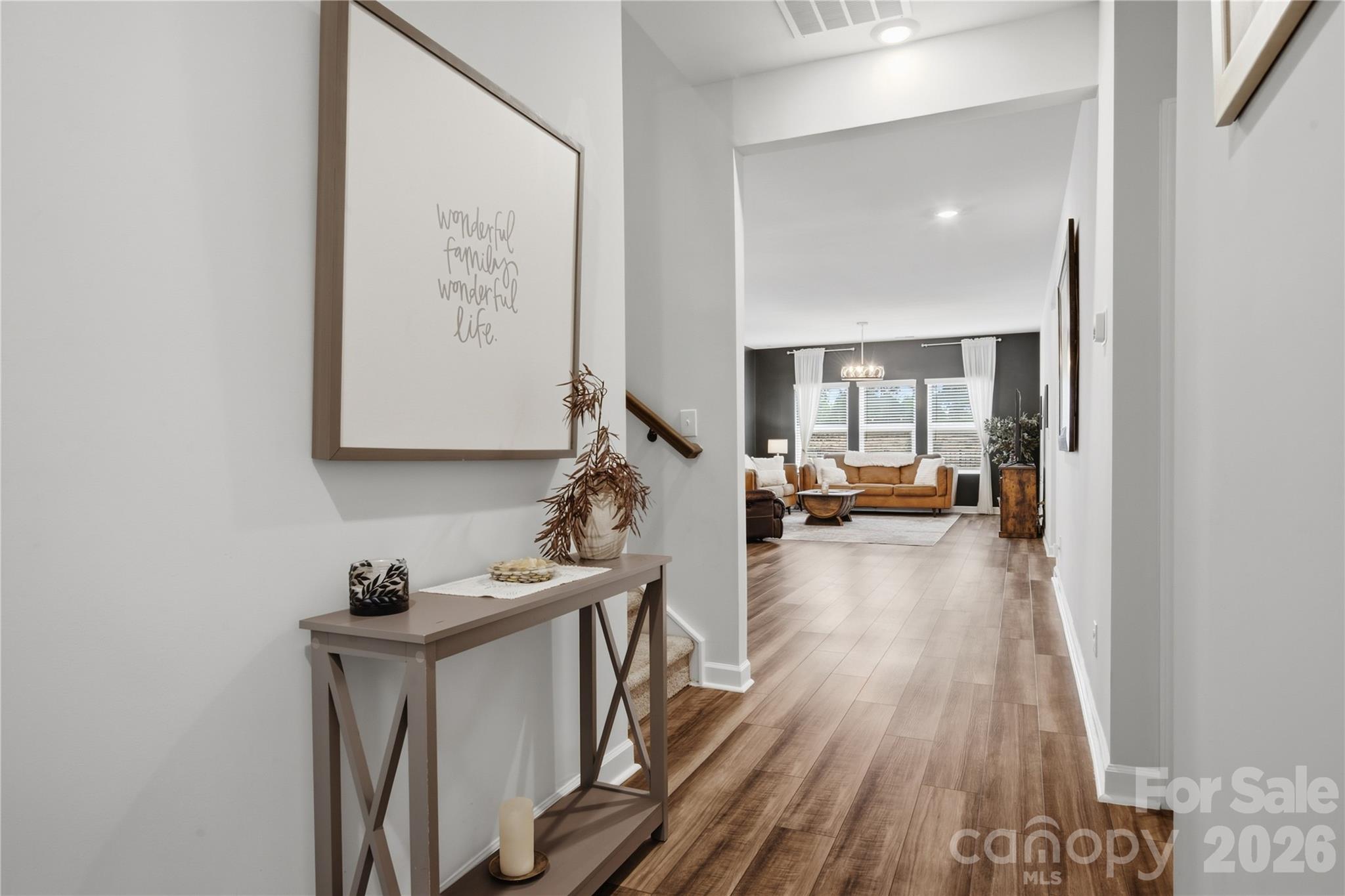 Entry hallway with wood-look floors and console table leading to a living room with a tan sofa.