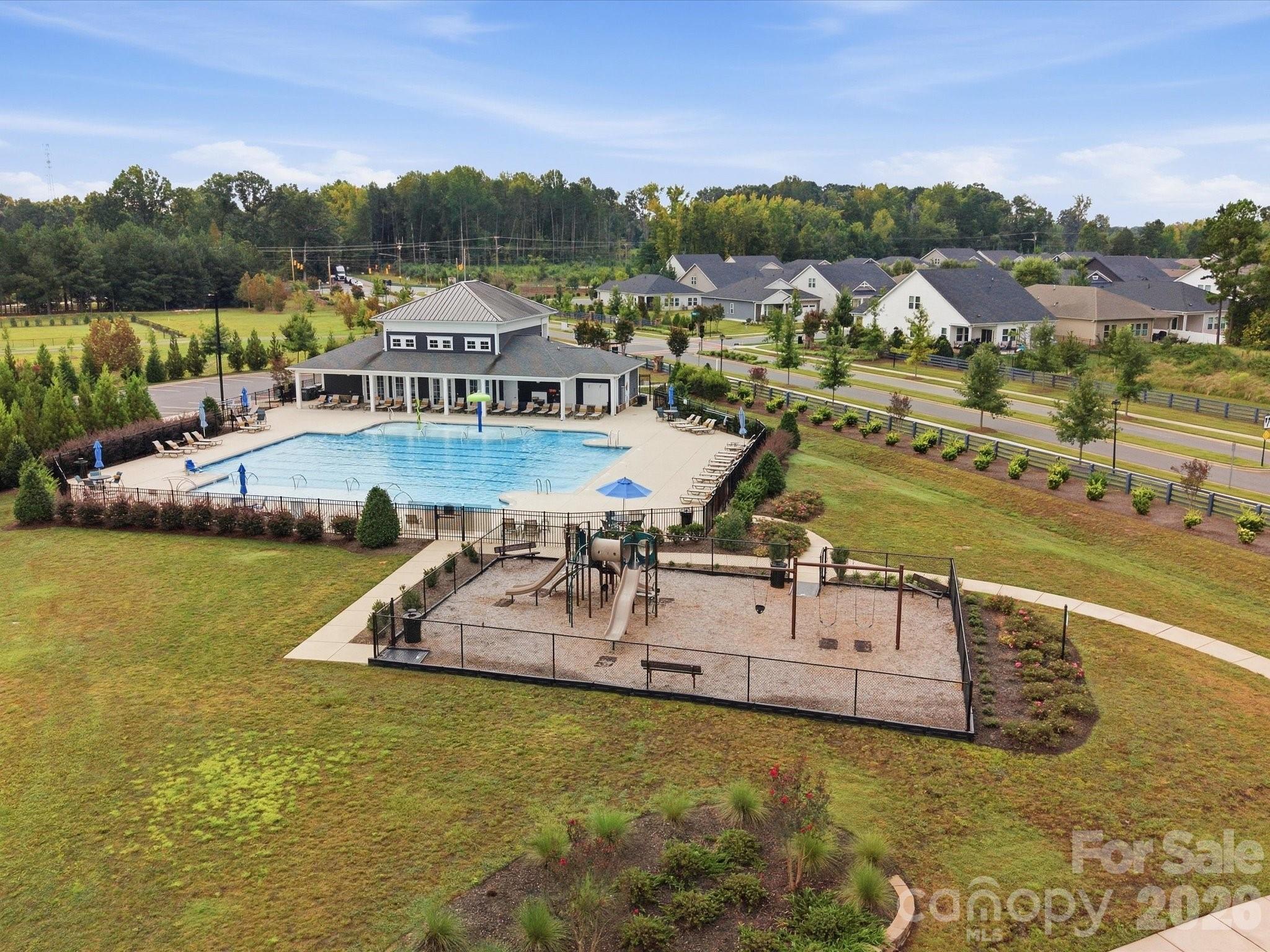 Aerial view of a community pool, clubhouse, and fenced playground among nearby homes.
