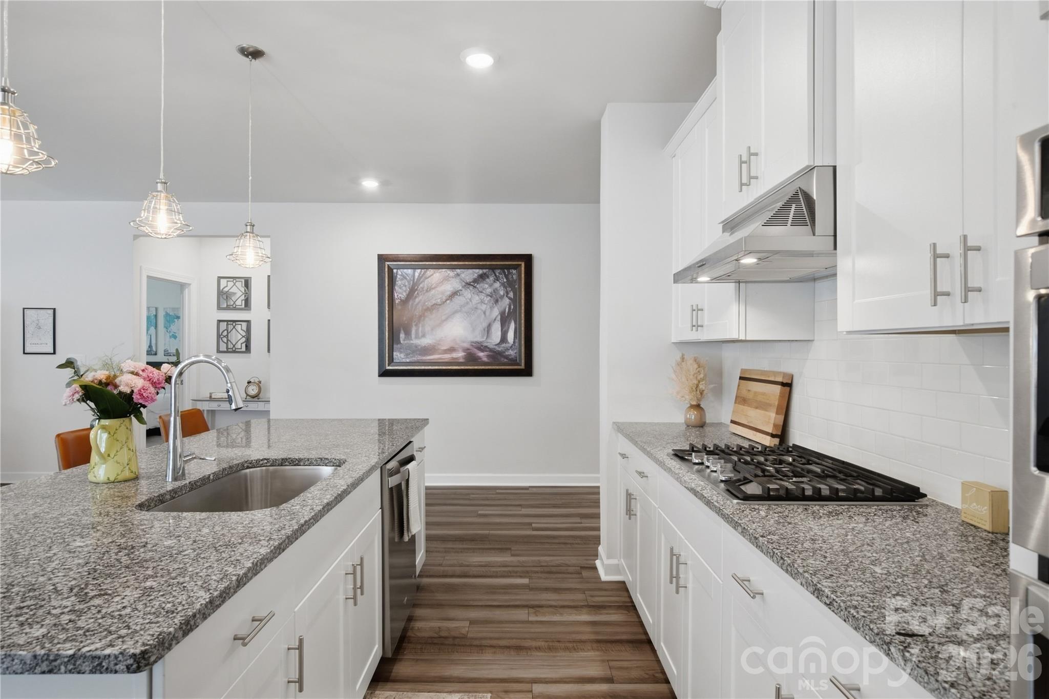 Bright kitchen with white cabinets, granite counters, a large sink island, and a gas cooktop.