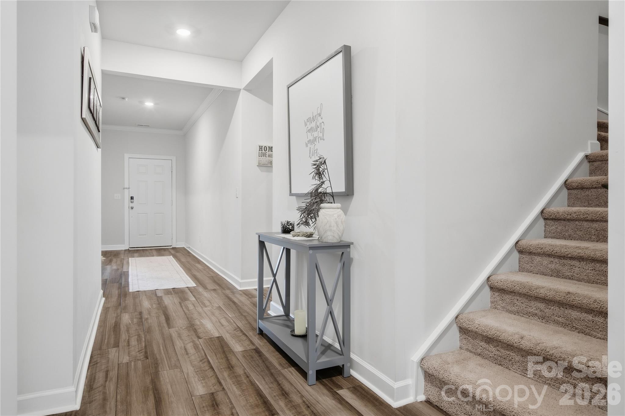 Staged entry hall with wood-look floors, a gray console table, and carpeted stairs.