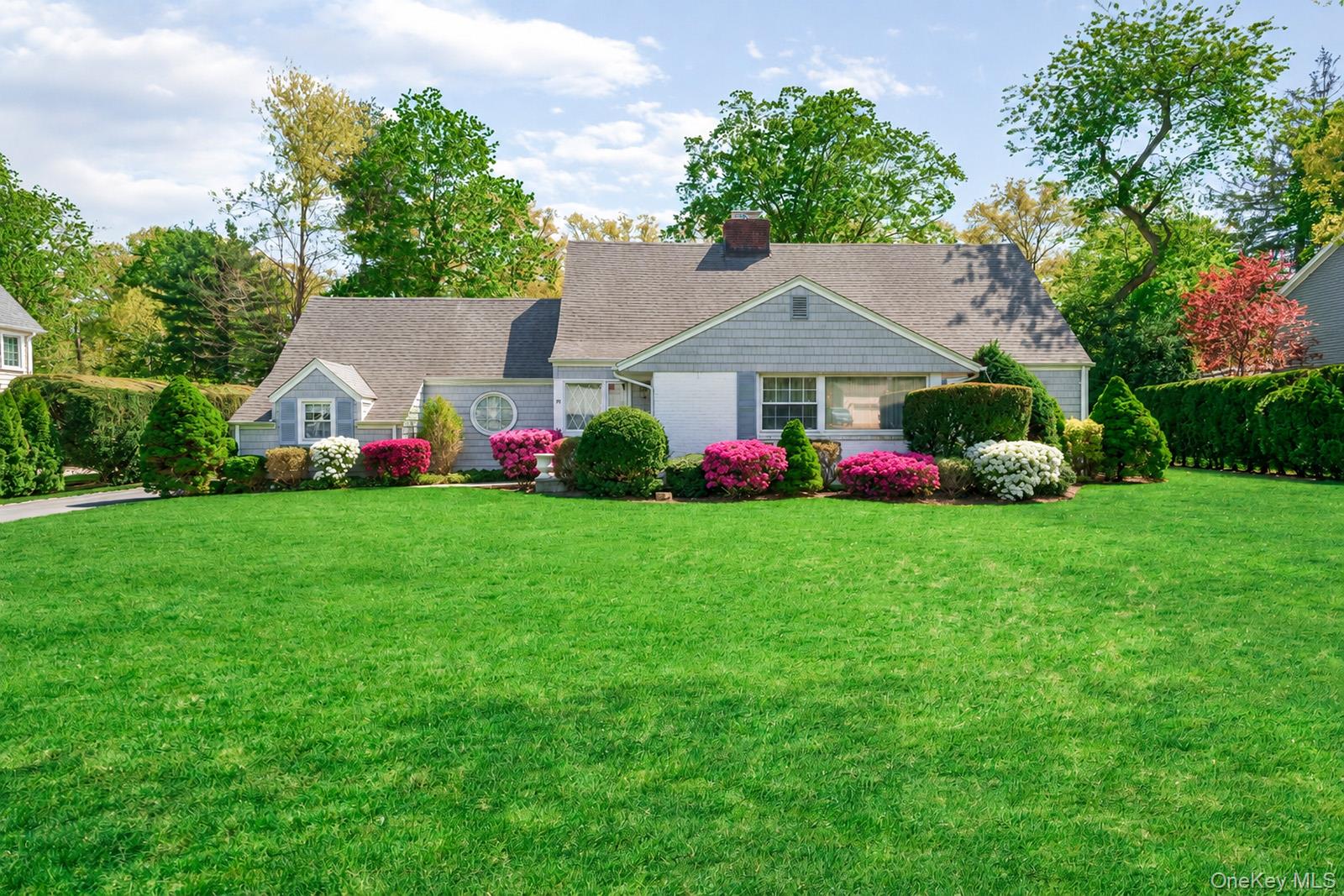 88 Brook Street home with gray shingles, a broad lawn, and colorful foundation gardens.