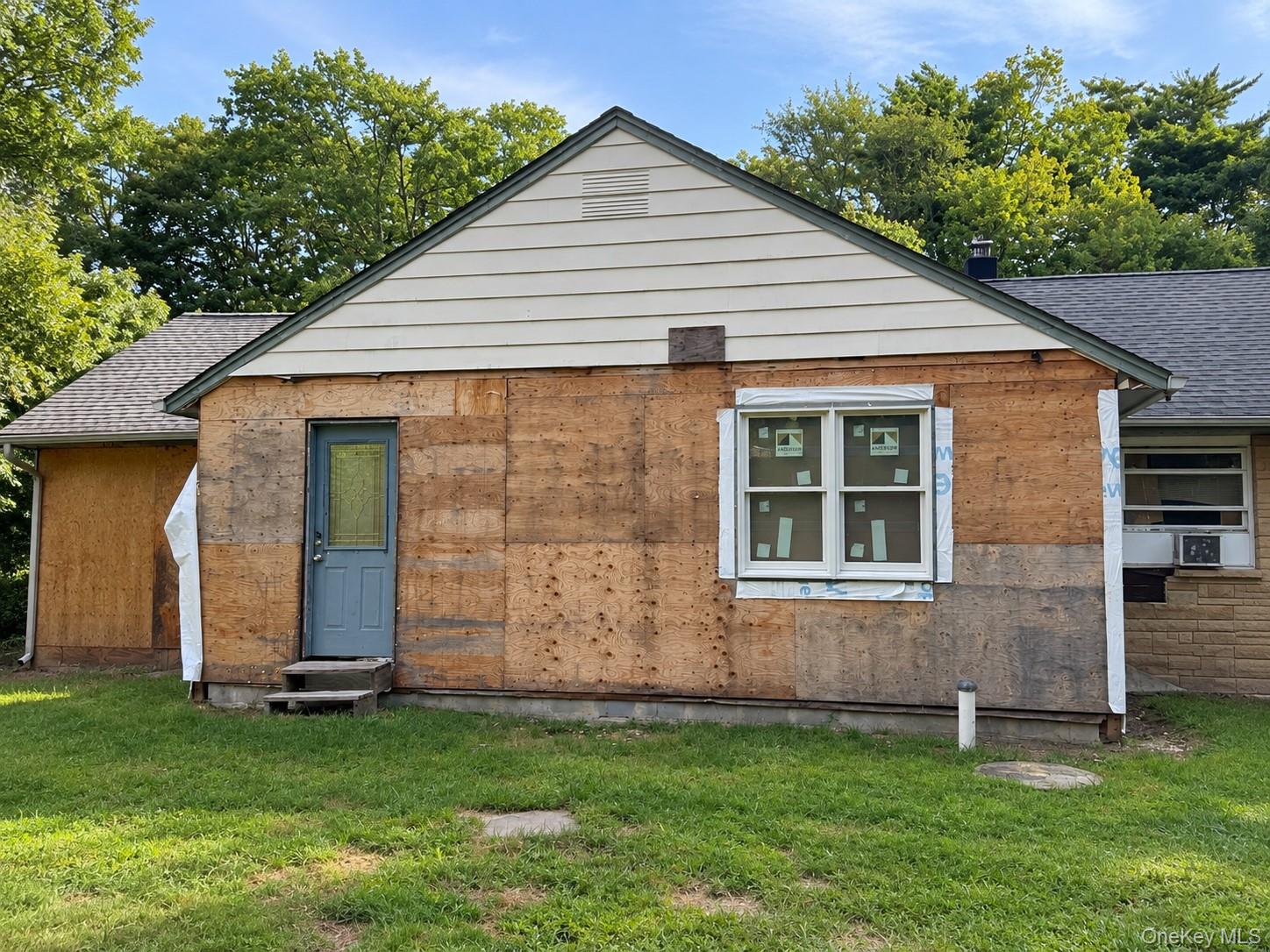 House under construction with plywood siding, a blue front door, and a newly installed window.