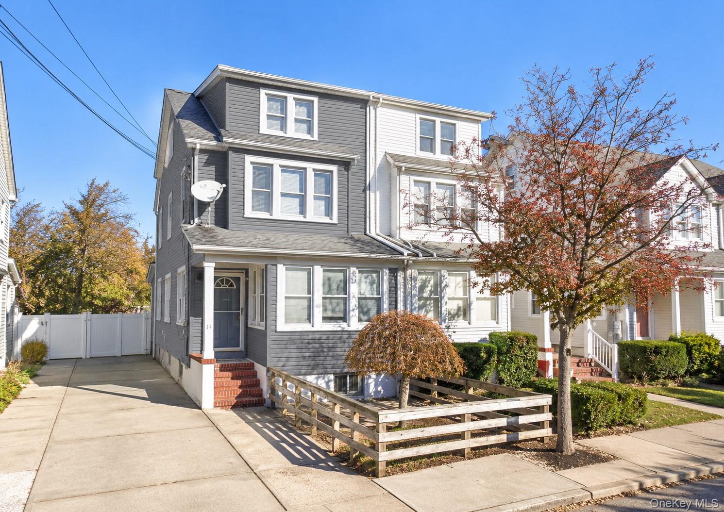 Gray and white multi-story home with a driveway, front steps, and autumn trees.