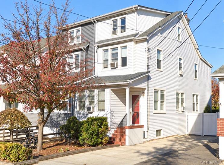 White multi-story house with a red front door, bay windows, and paved driveway.