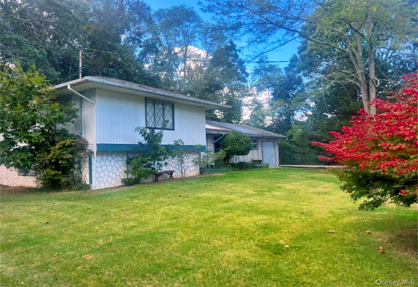 White home with a stone-patterned lower facade, broad lawn, and red flowering shrubs.