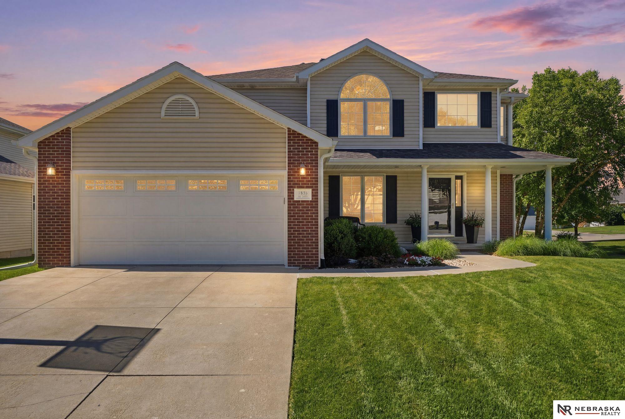 Two-story gray home with brick accents, a double garage, and a covered porch at dusk.
