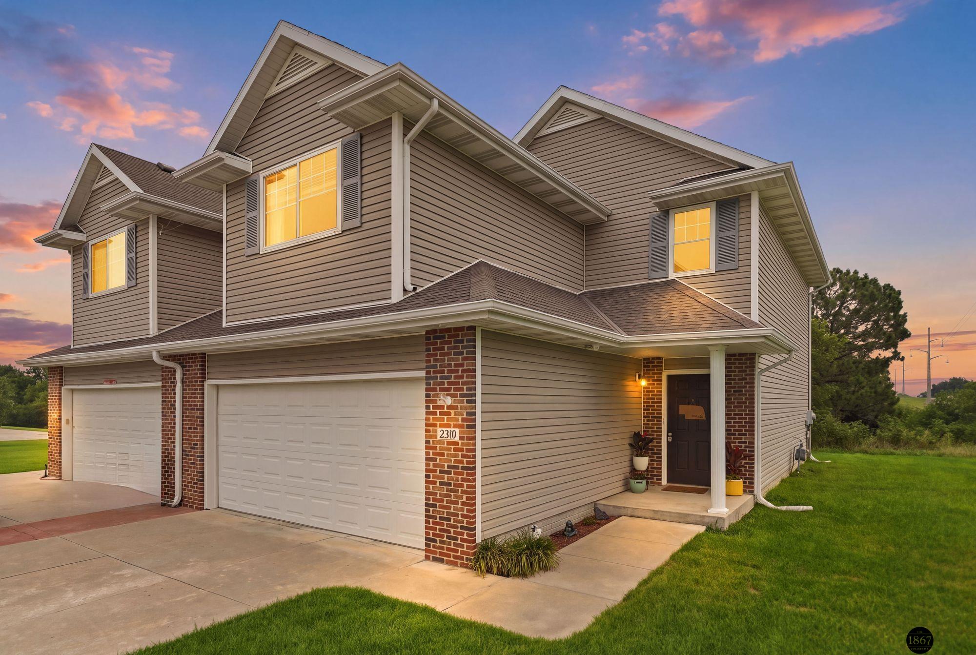 Two-story taupe-sided home with brick accents and two garage doors at dusk.