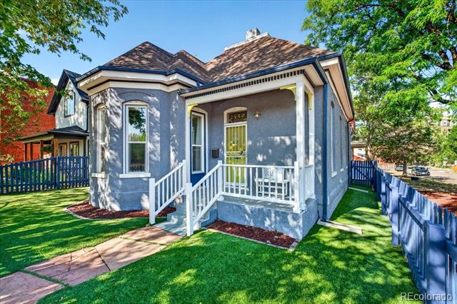 Gray house with a covered porch, white railings, and blue picket fence.