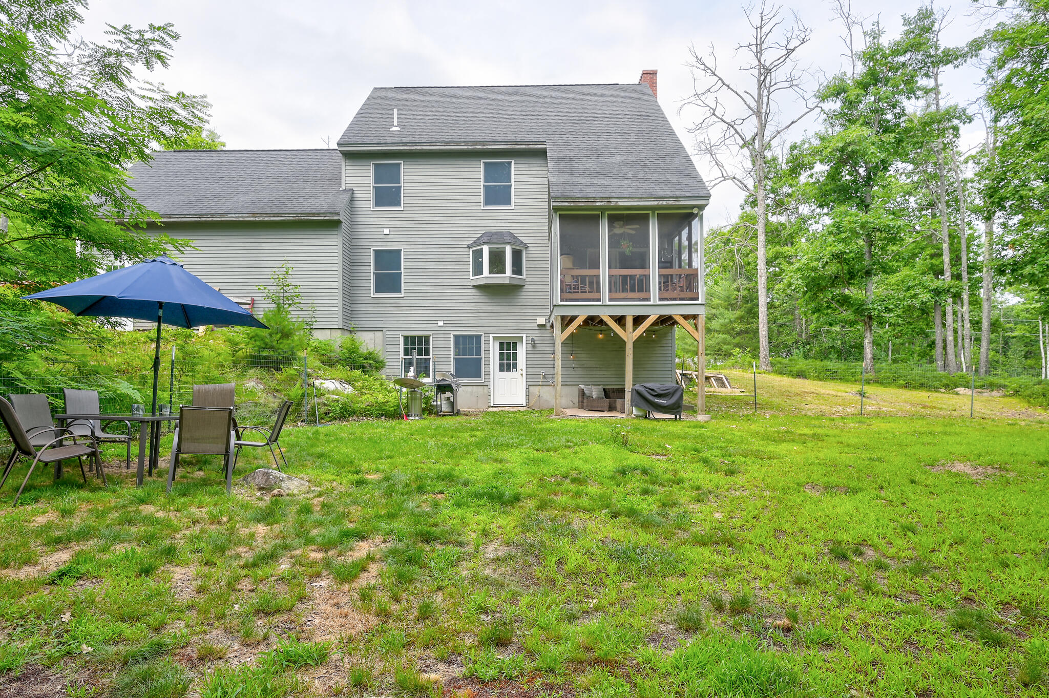 Rear of a gray house with a screened porch overlooking a grassy yard and patio.