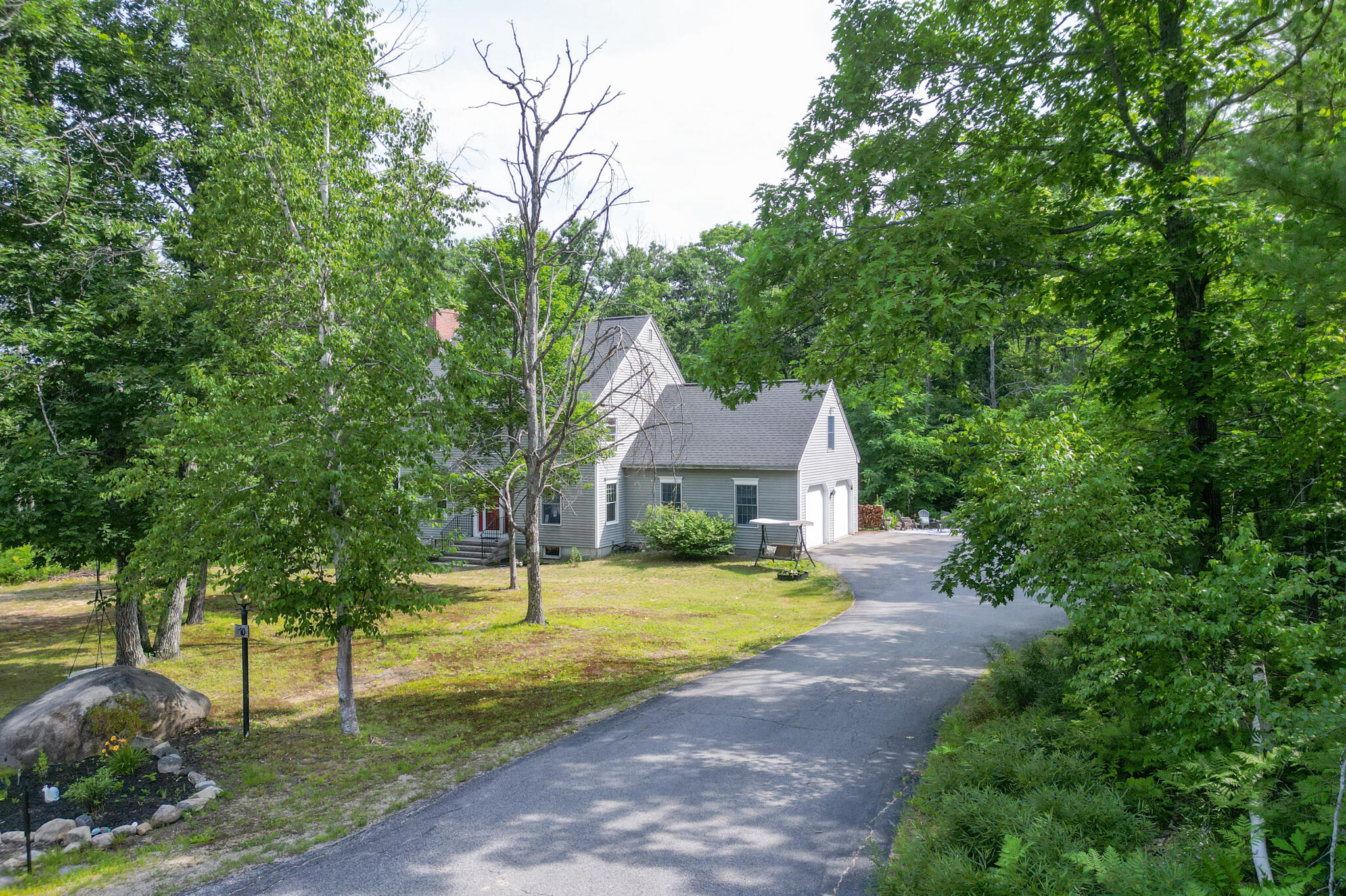 Gray house with attached garage, set among trees beside a curved driveway.