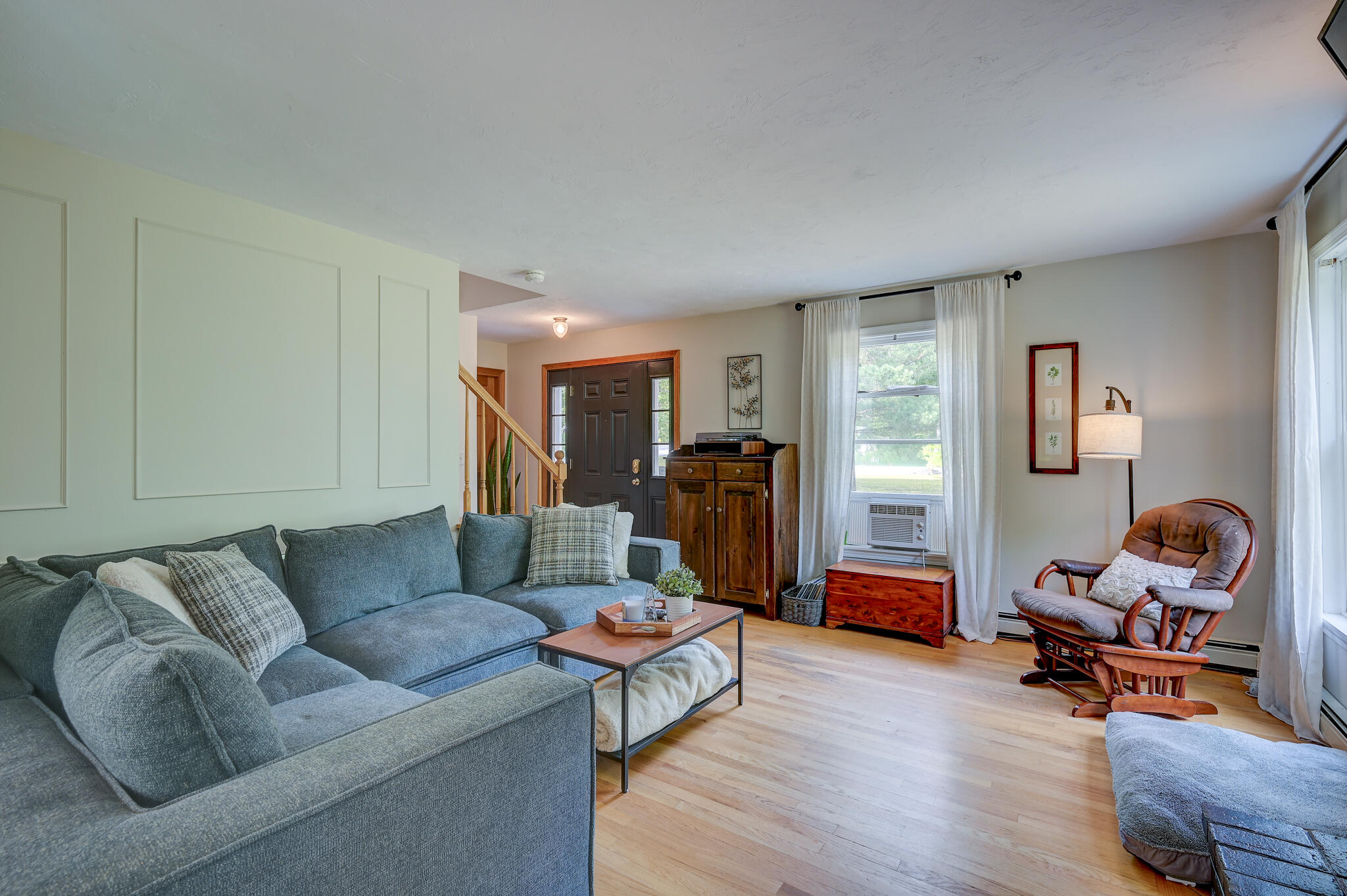 Living room with a blue sectional, wood furnishings, and a curtained window beside the front door.