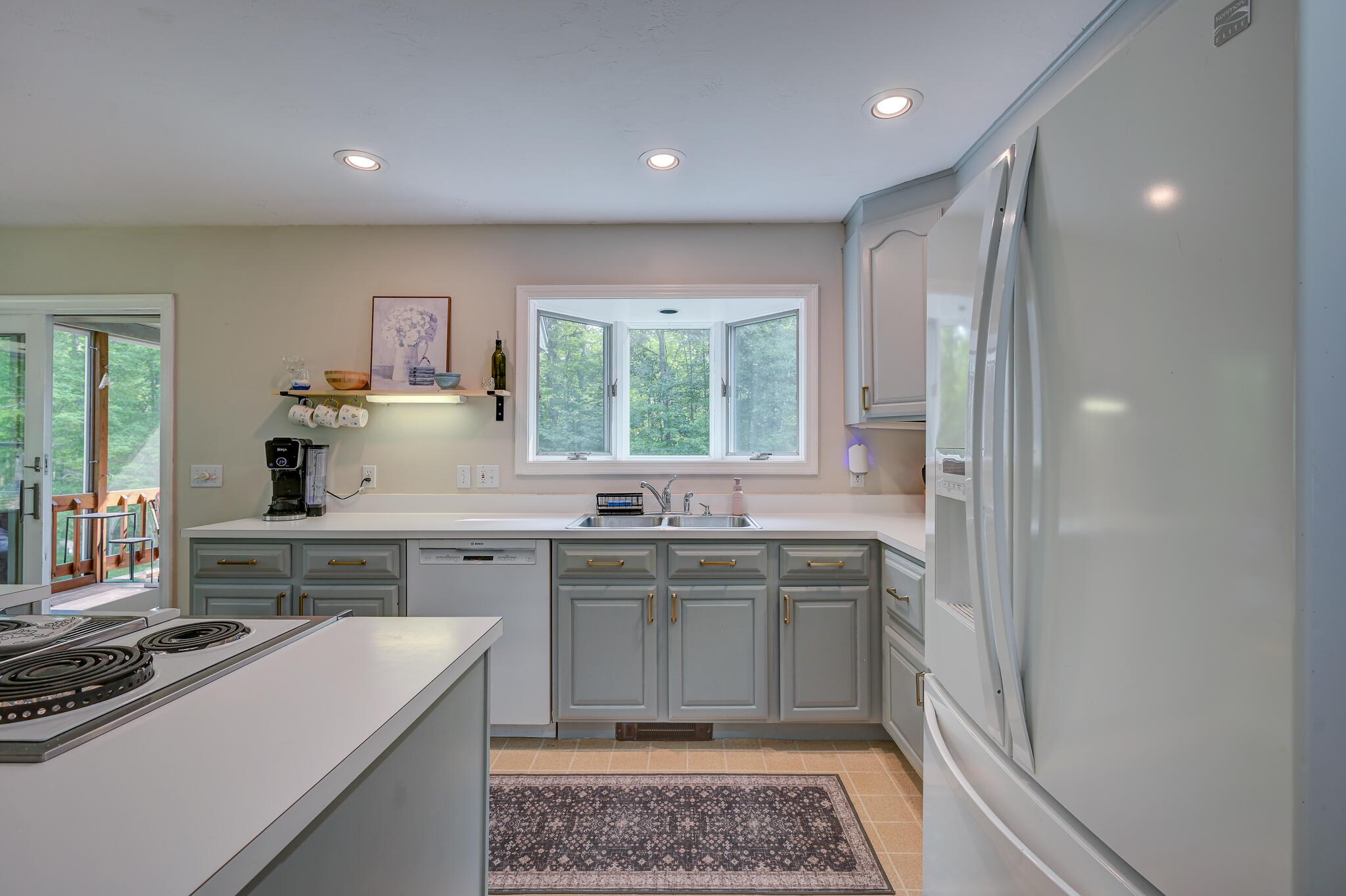 Kitchen with gray cabinets, a double sink beneath a bay window, and a large refrigerator.