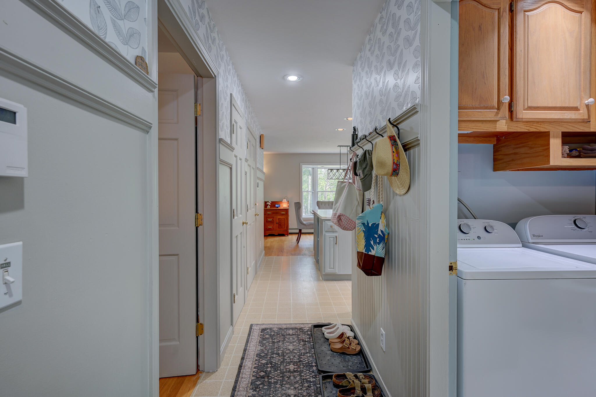 Mudroom hallway with coat hooks, tiled floor, shoe trays, and an adjoining laundry area.