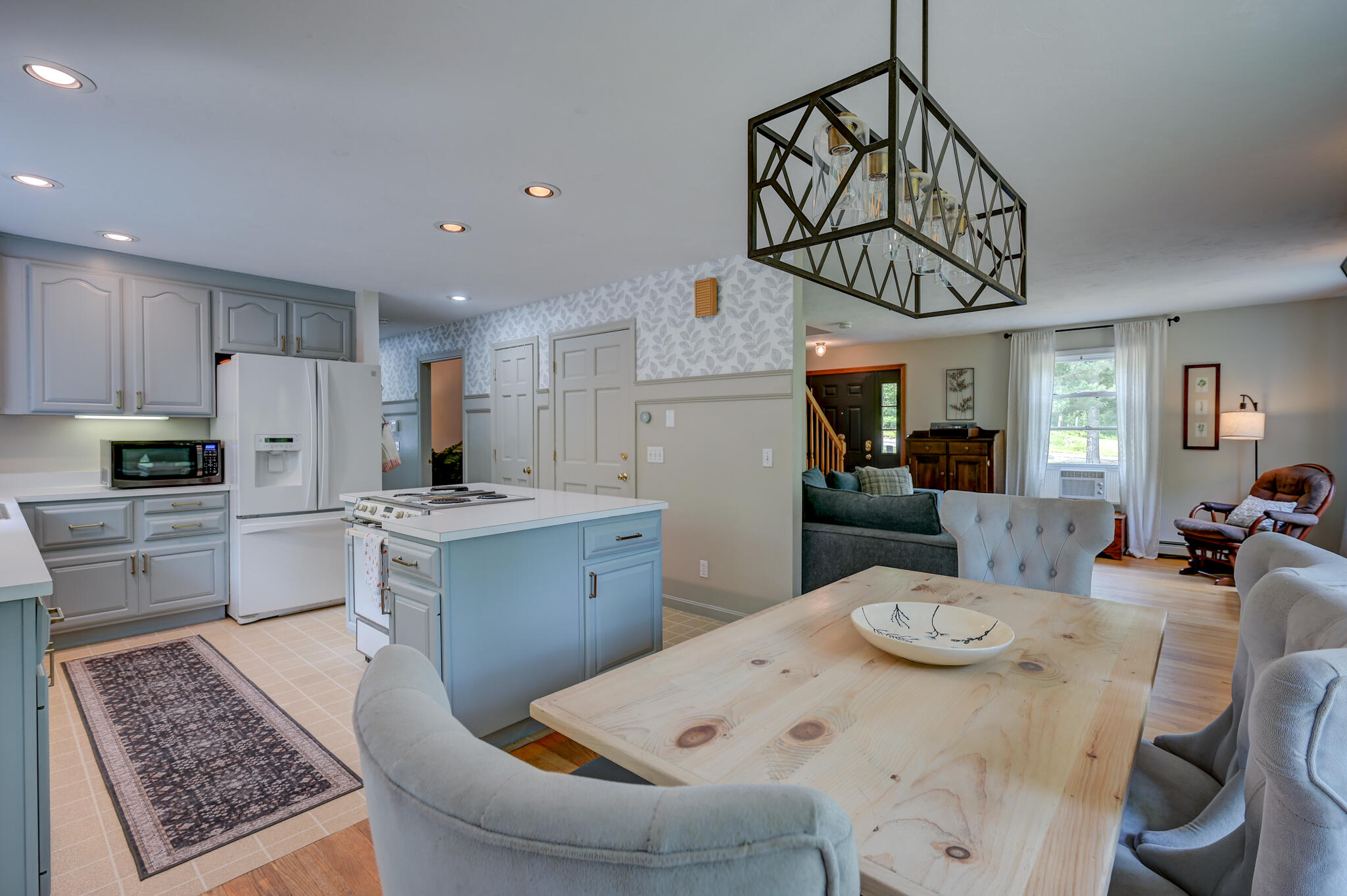 Open kitchen and dining area with a blue island, pale wood table, and living room beyond.