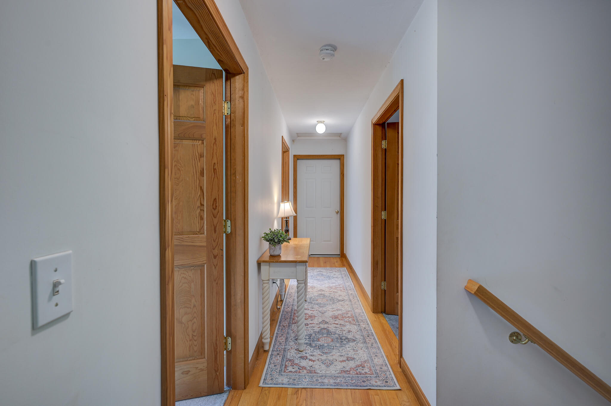 Hallway with honey-colored wood trim, patterned runner, and console table beneath a lamp.