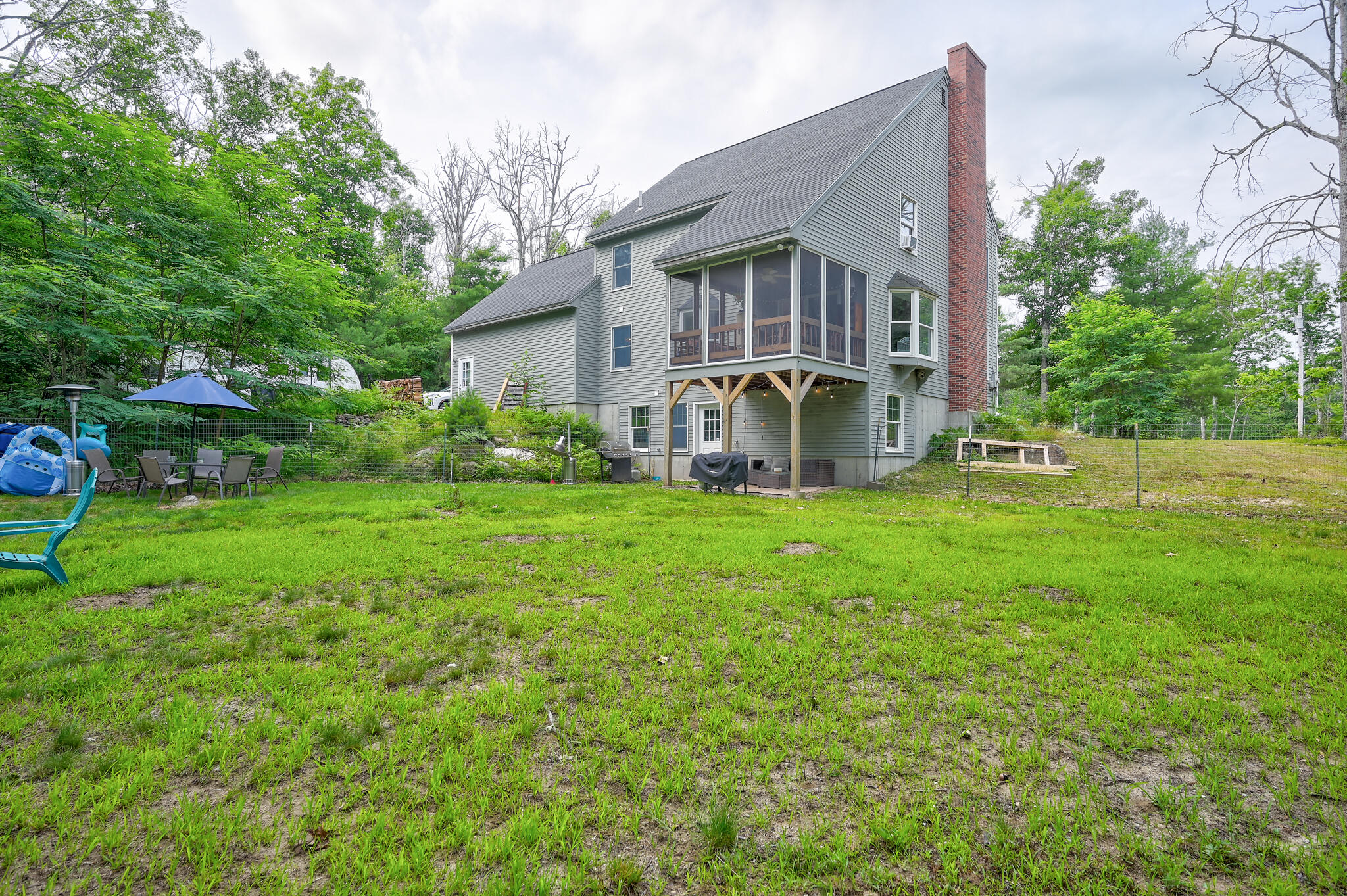 Rear exterior of a gray house with a screened porch, brick chimney, and grassy yard.