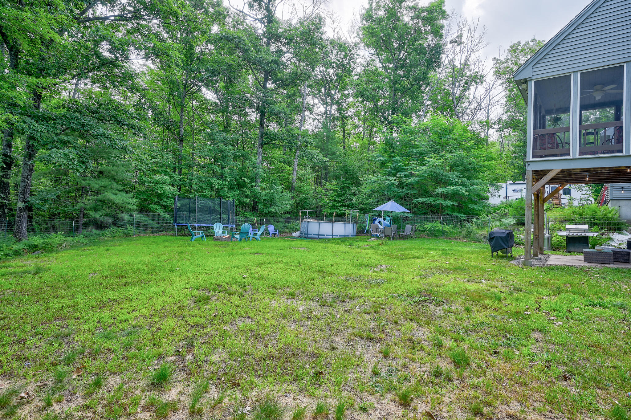 Backyard with above-ground pool, lawn, outdoor seating, and a raised screened porch beside woods.