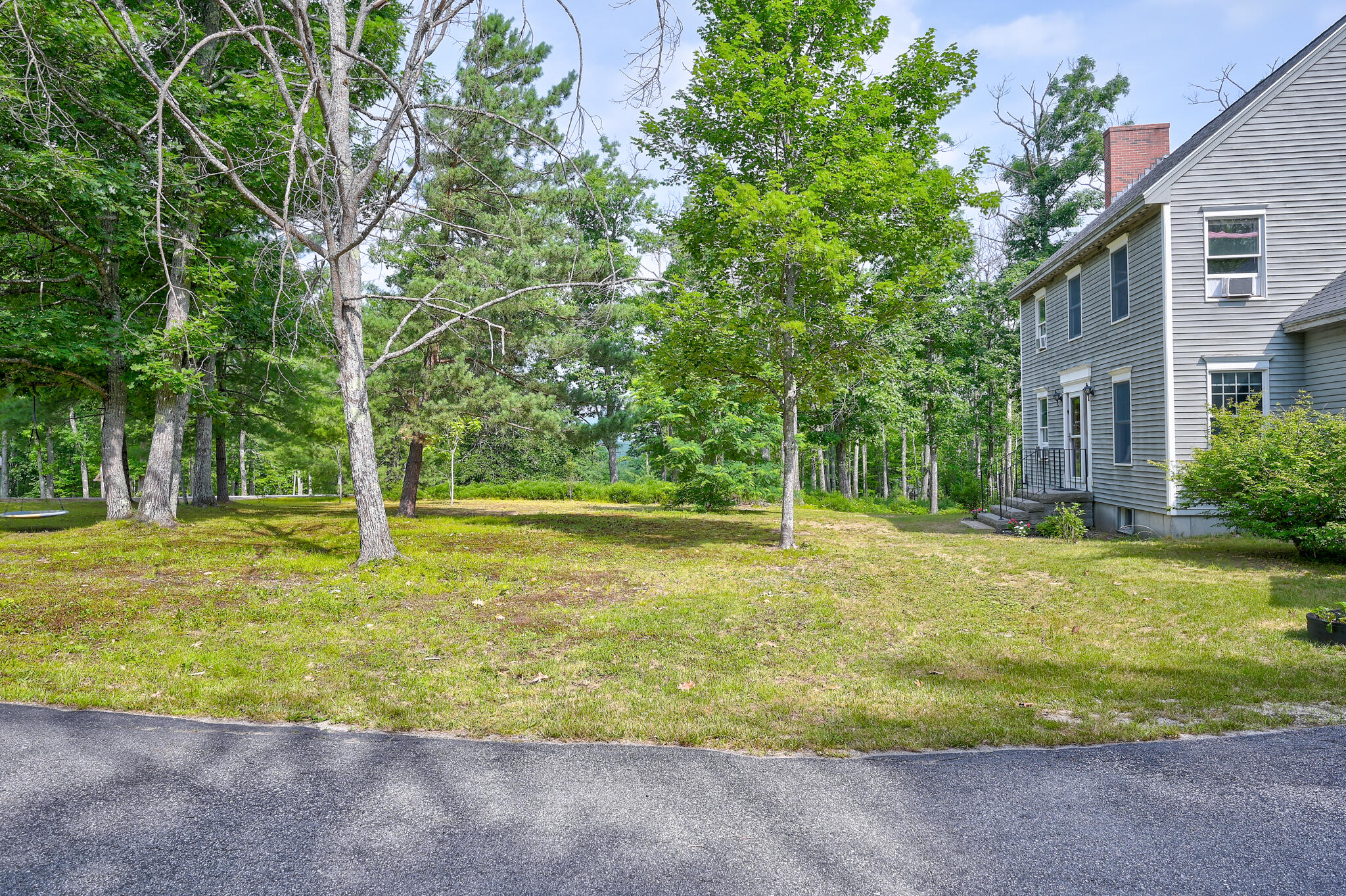 Gray-sided house beside a grassy yard shaded by mature trees.