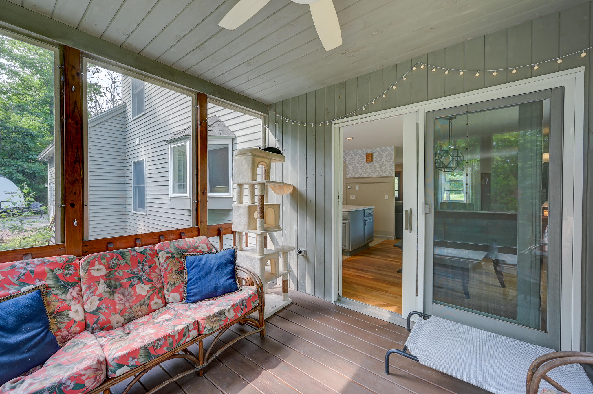 Covered porch with floral seating, a cat tree, string lights, and sliding glass doors.