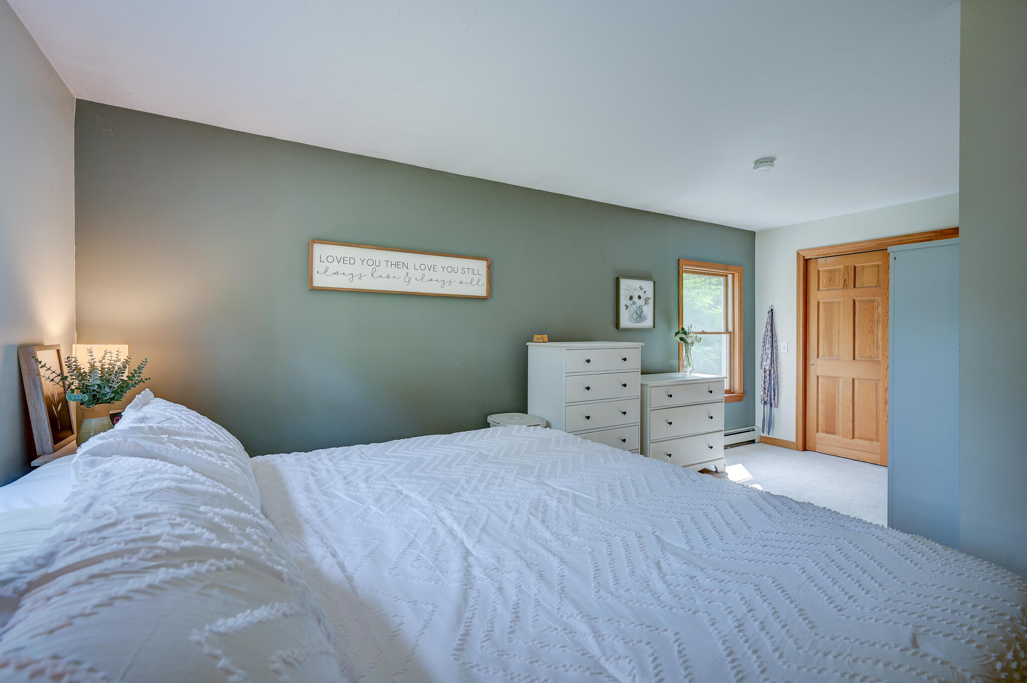 Bedroom with a white quilted bed, sage green wall, and wooden door.