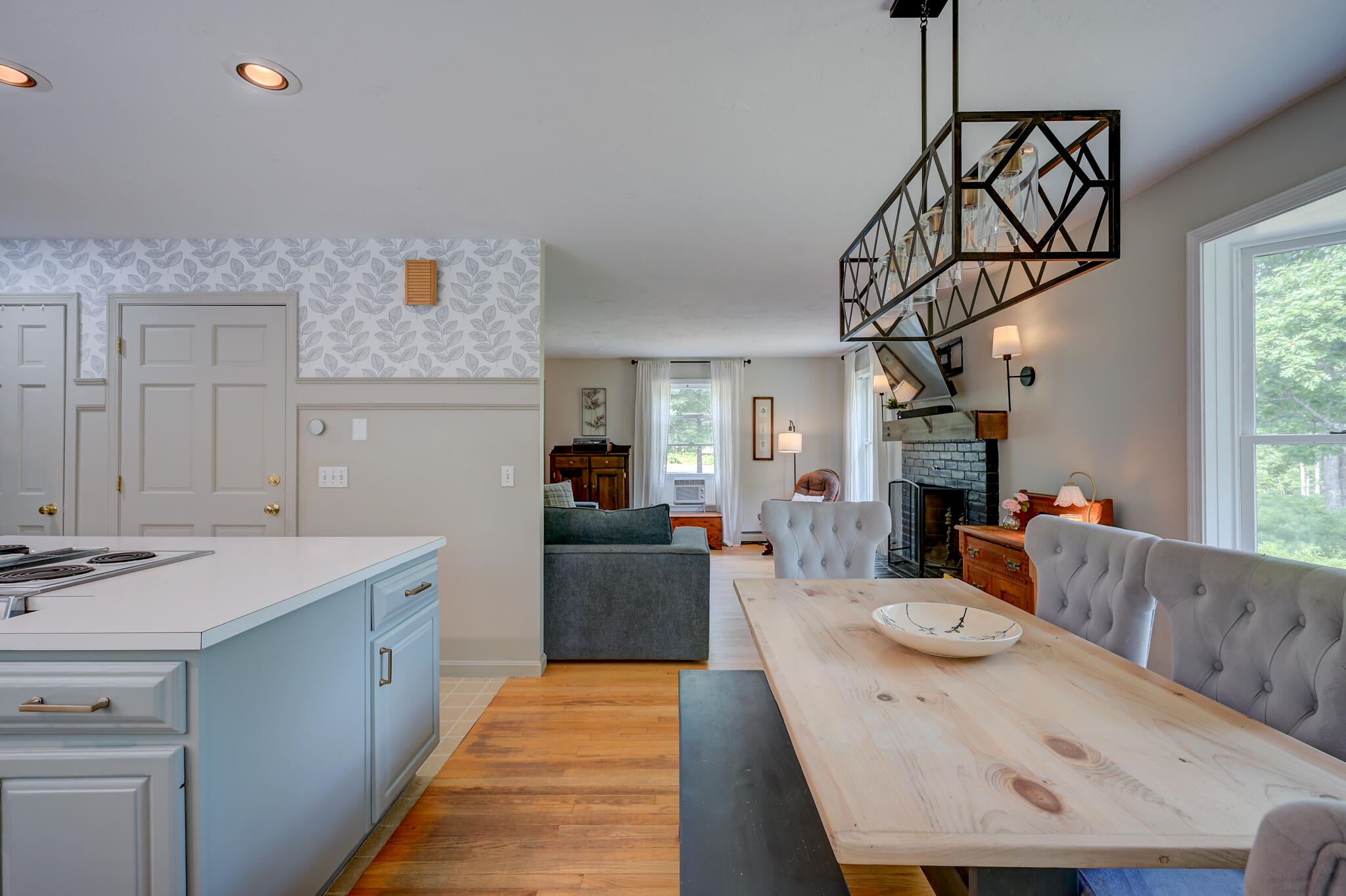 Open-plan kitchen and dining area with a long wood table, pale blue island, and stone fireplace.