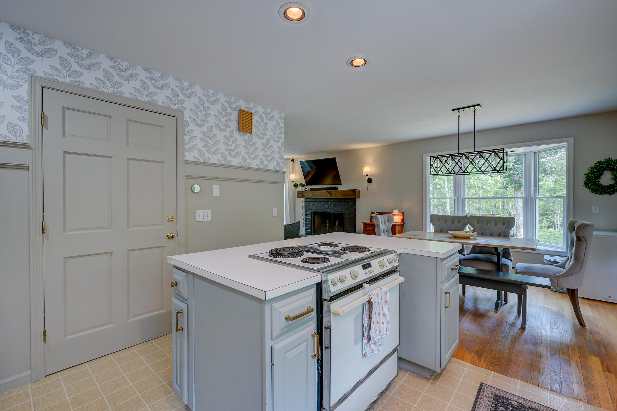 Kitchen with a central island and electric range opening to a dining nook with large windows.