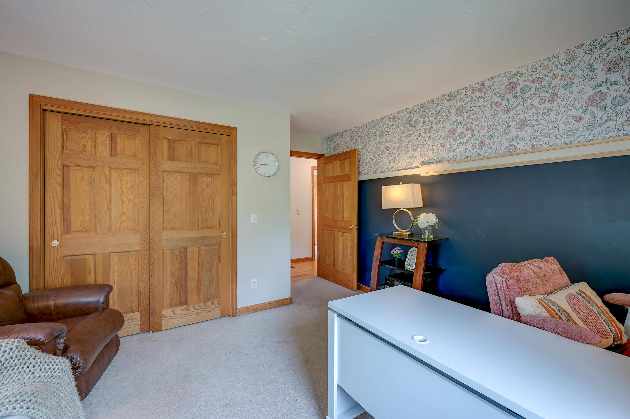 Furnished room with wooden closet doors, a navy accent wall, and patterned floral wallpaper.