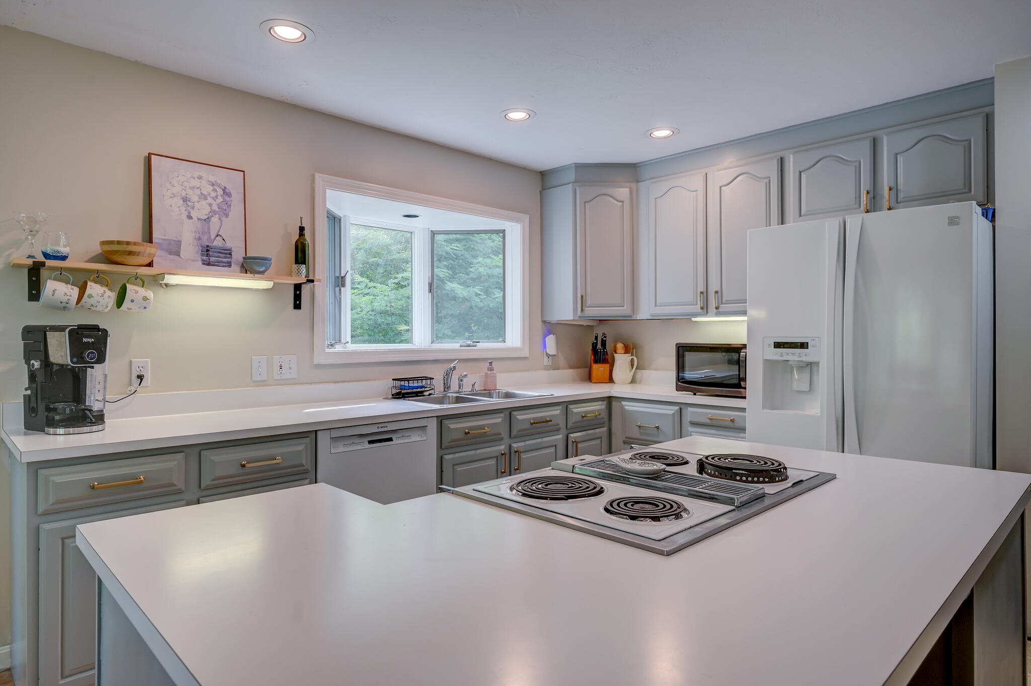 Kitchen with gray cabinets, white counters, a large island cooktop, and a window over the sink.