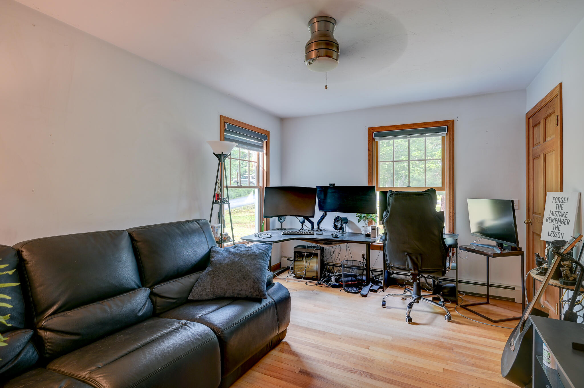 Home office with a multi-monitor workstation, black leather sofa, and wood-trimmed windows.