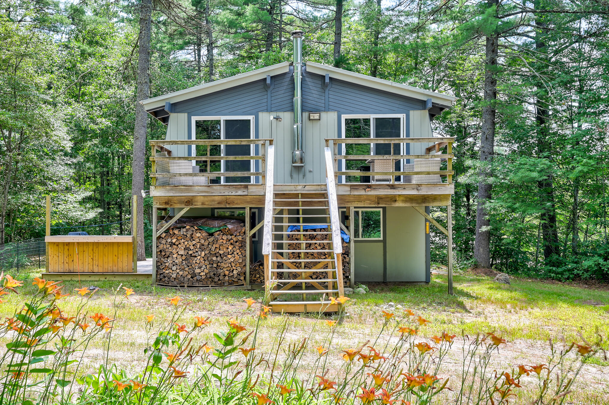 Raised cabin with a wooden deck and central stairs, surrounded by trees and orange flowers.