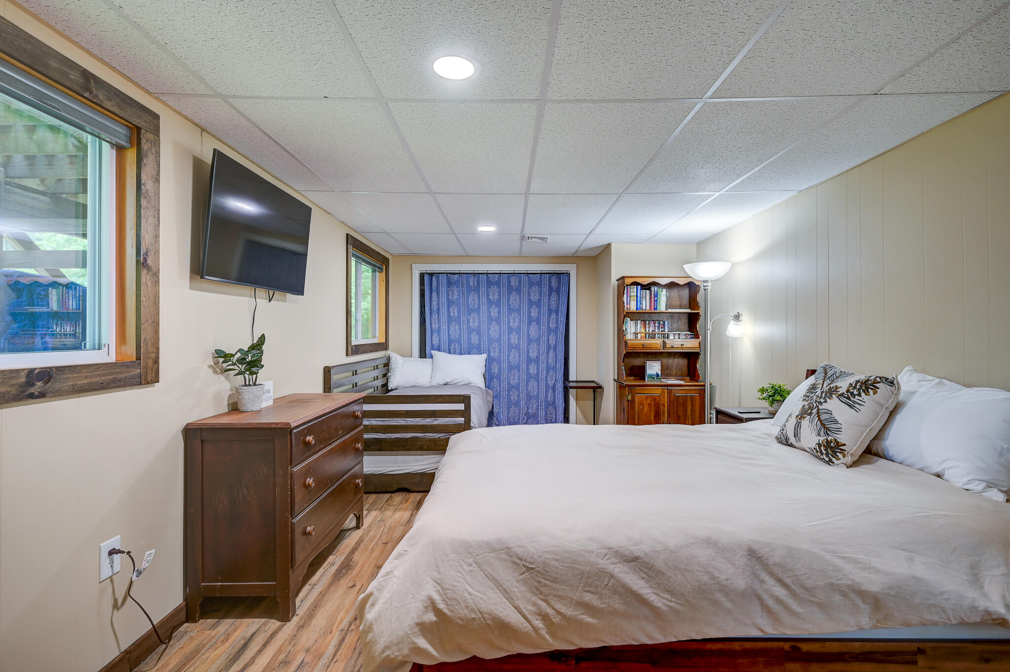 Bedroom with two beds, rustic wood trim, a wall-mounted TV, and a wooden bookcase.