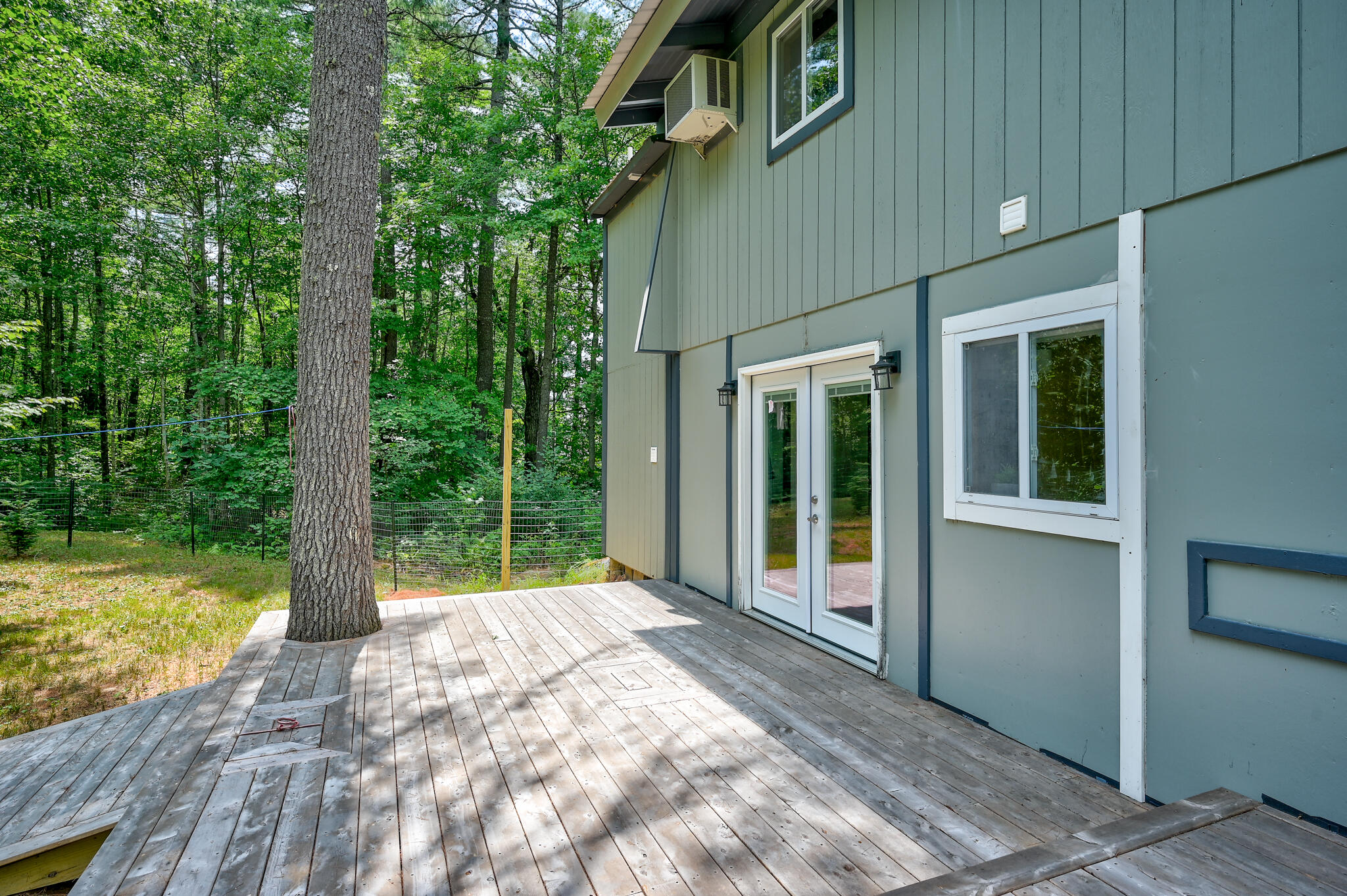 Wooden deck beside a blue-gray house, with glass doors and a mature tree growing through the decking.