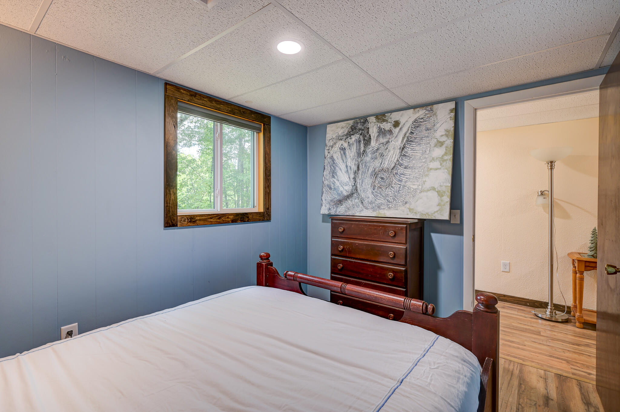 Bedroom with blue paneled walls, a dark wood bed, and a dresser beneath elephant artwork.
