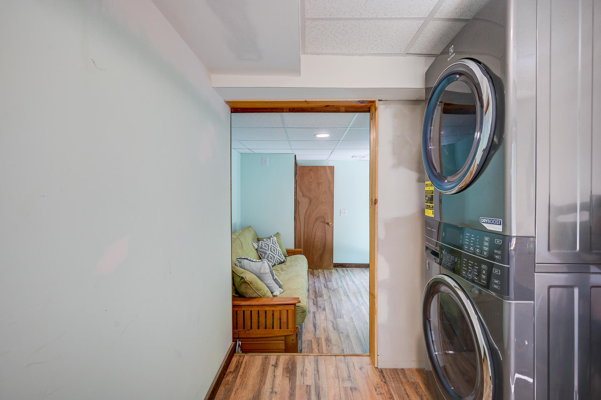 Laundry area with stacked washer and dryer beside a doorway to a small sitting area.