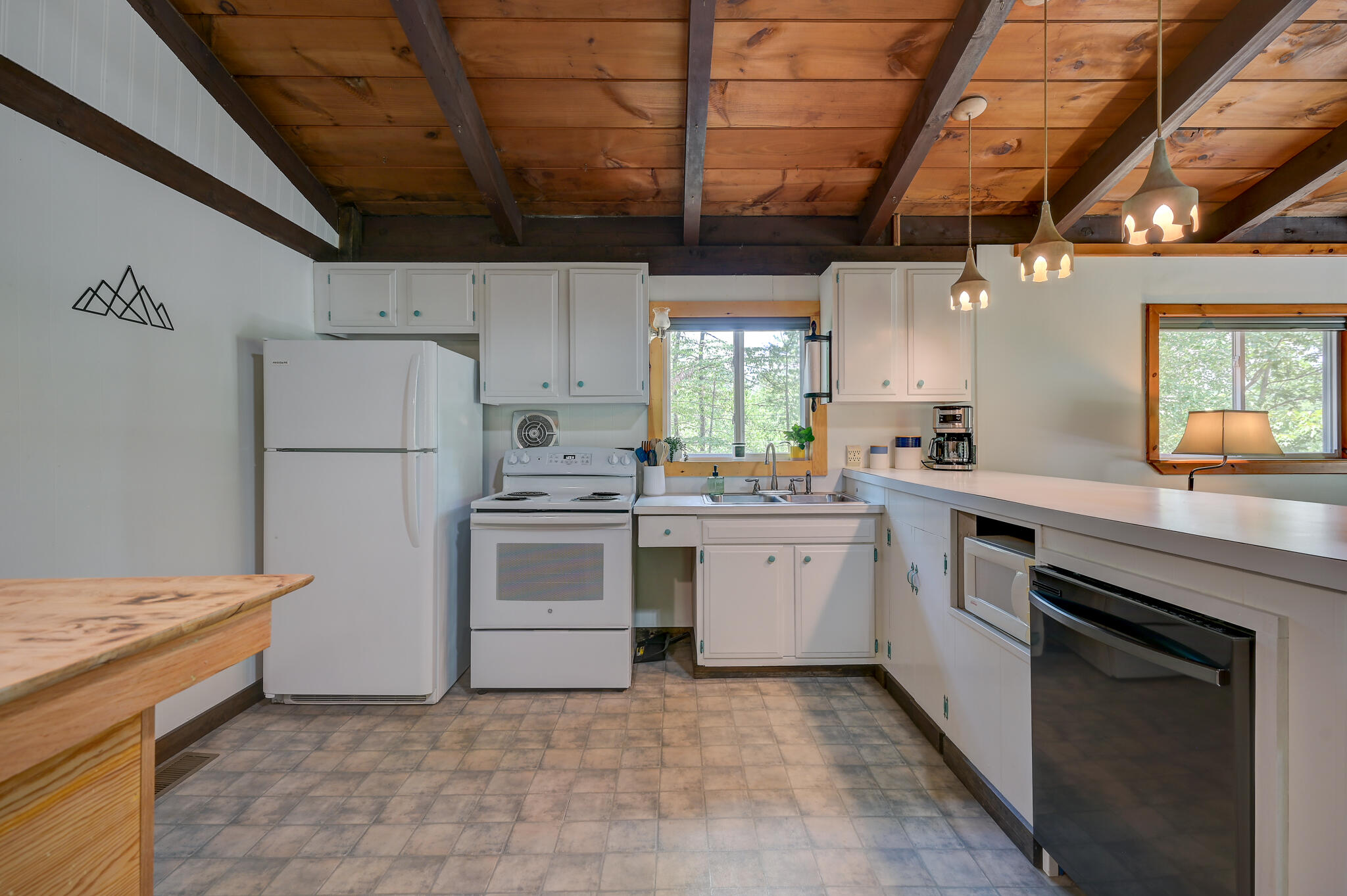 Kitchen with white appliances and cabinets beneath a vaulted, exposed wood-beam ceiling.