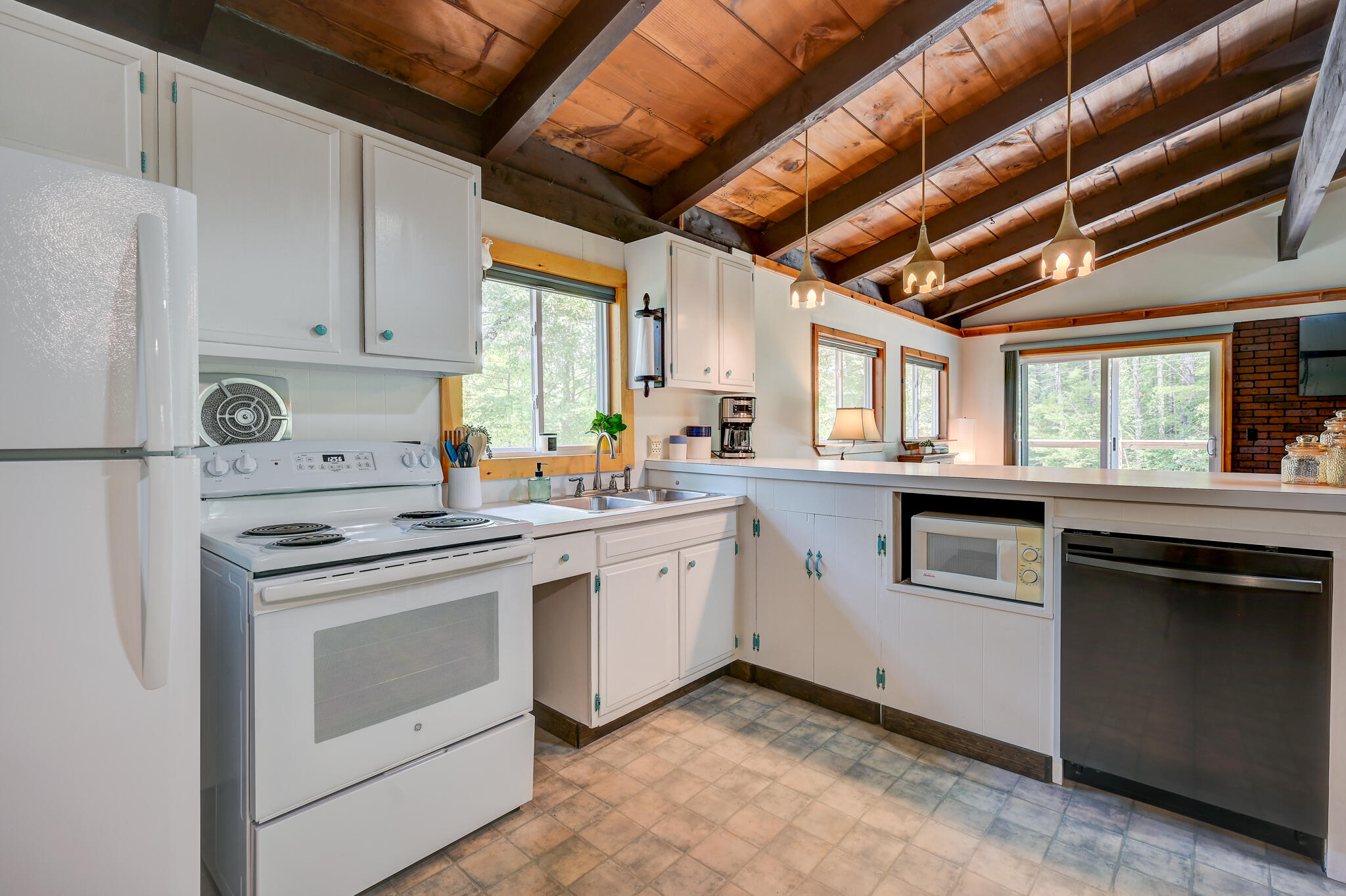 Kitchen with white cabinets, stainless dishwasher, and a vaulted wood-beam ceiling.