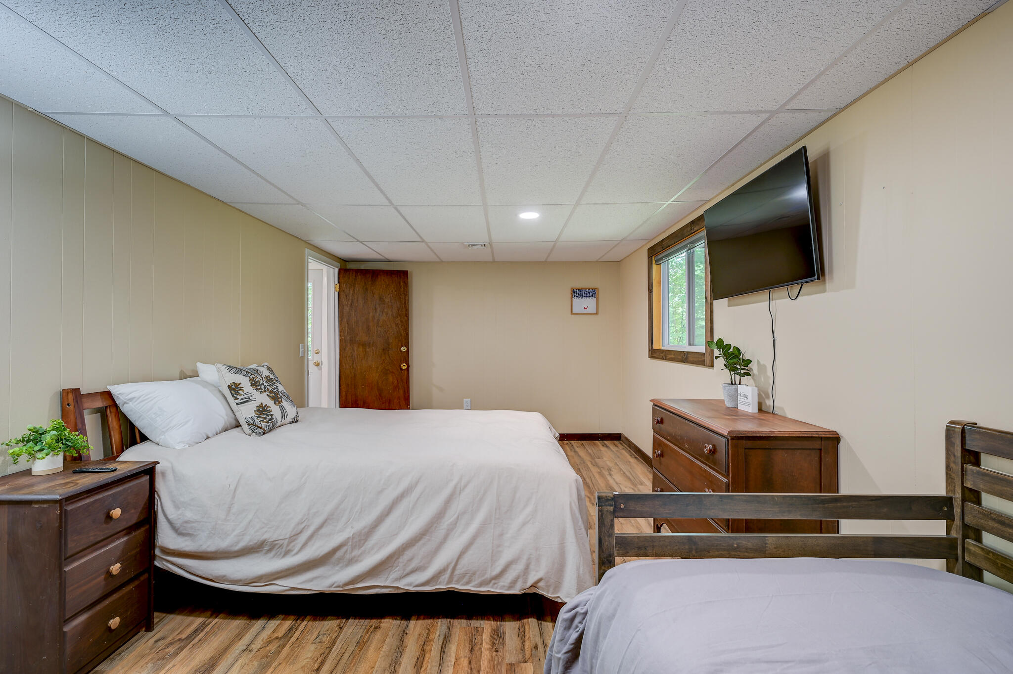 Bedroom with two beds, wood-look flooring, wooden dressers, and a wall-mounted television.
