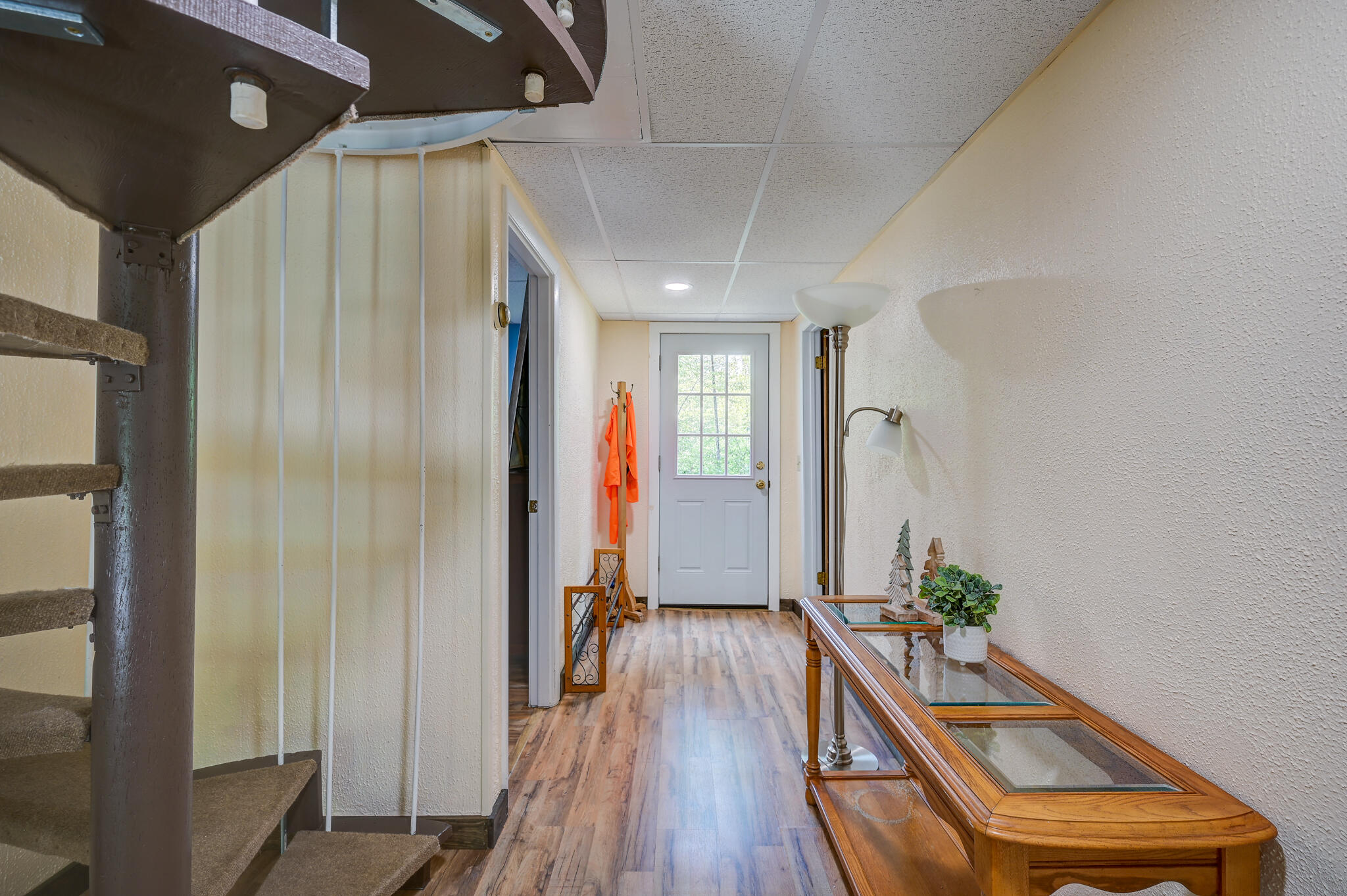 Entry hallway with a carpeted spiral staircase, glass-top console table, and white door.