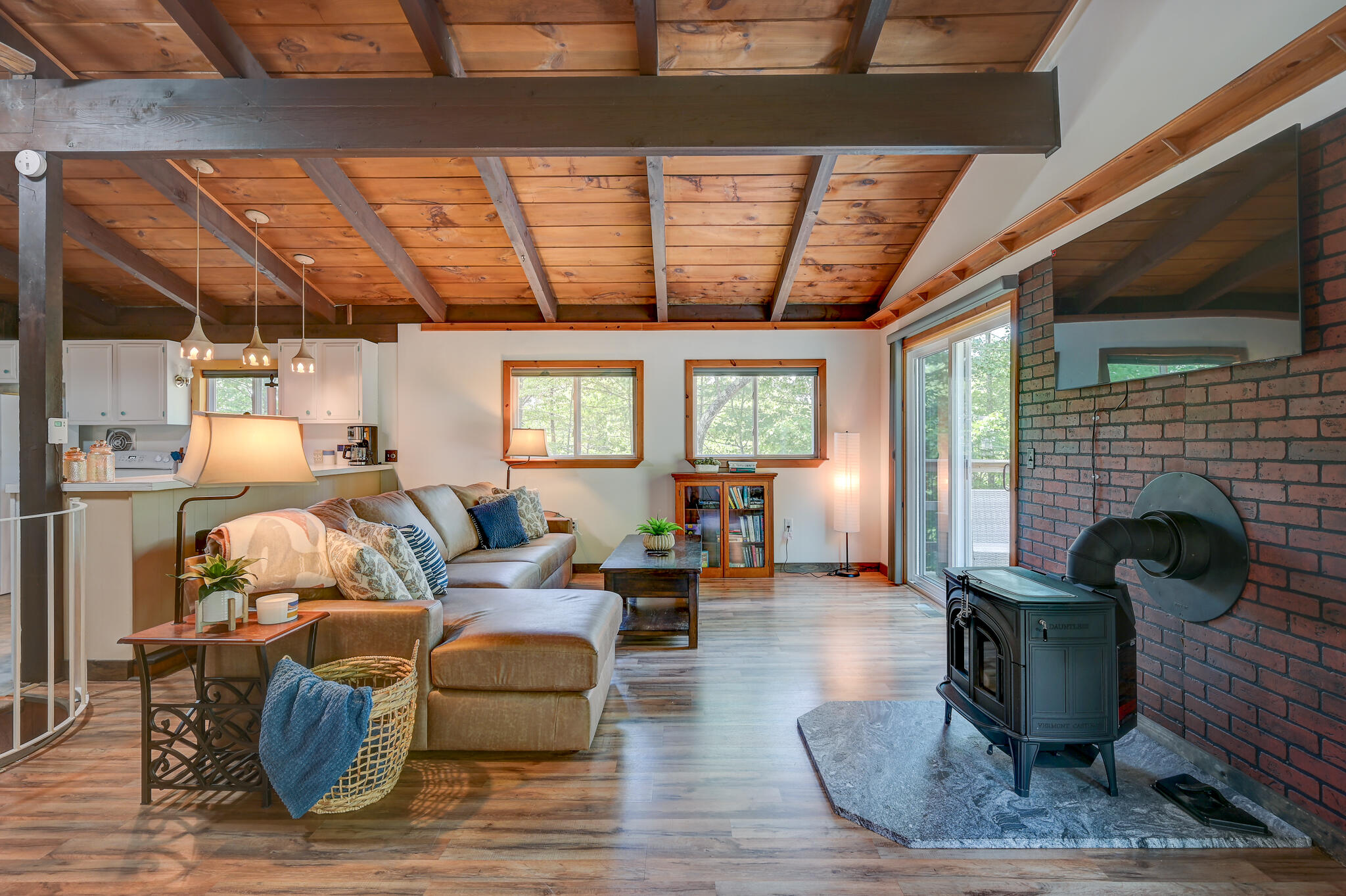 Living room with exposed wood ceiling, brick fireplace wall, wood stove, and sliding glass doors.