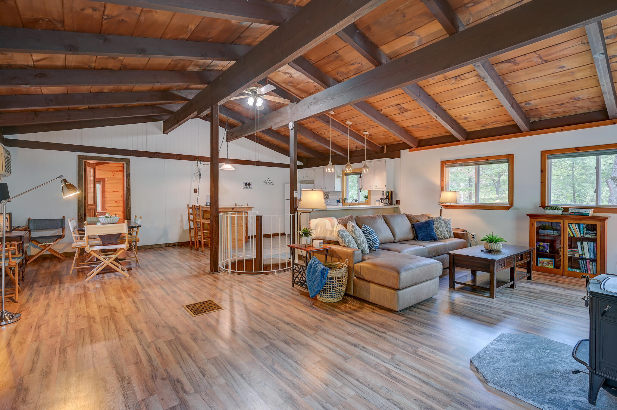 Open living and dining area with exposed timber beams, vaulted wood ceiling, and kitchen beyond.