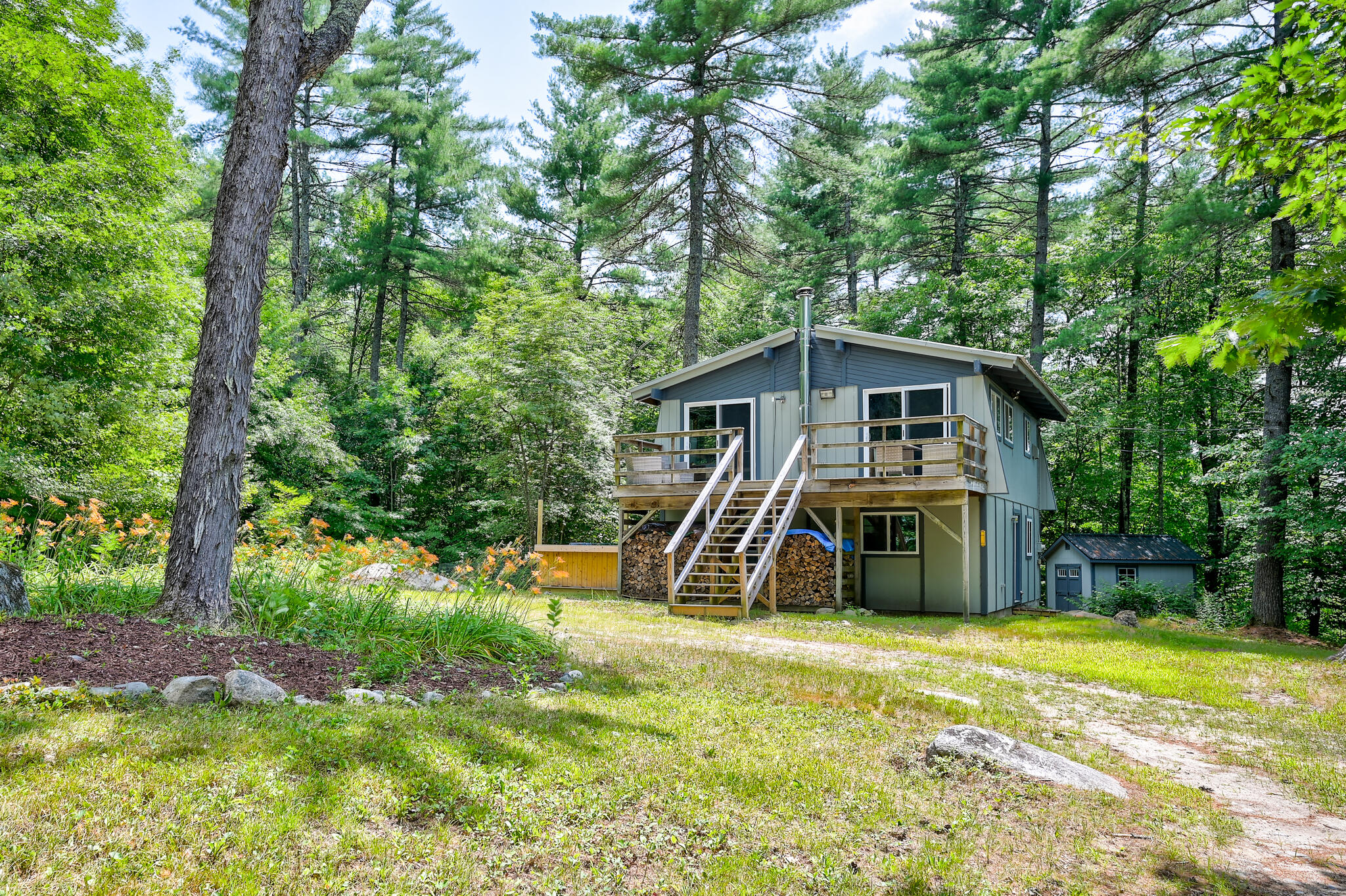Gray house with a raised deck and exterior stairs in a wooded setting.