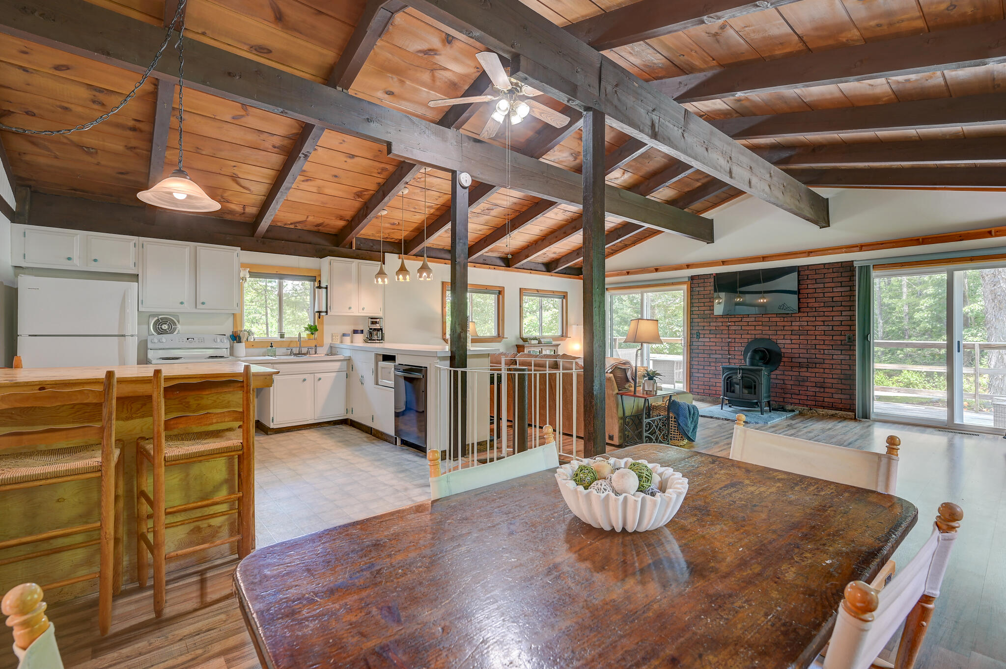 Open kitchen and living area with exposed wood beams, a brick fireplace, and dining table.