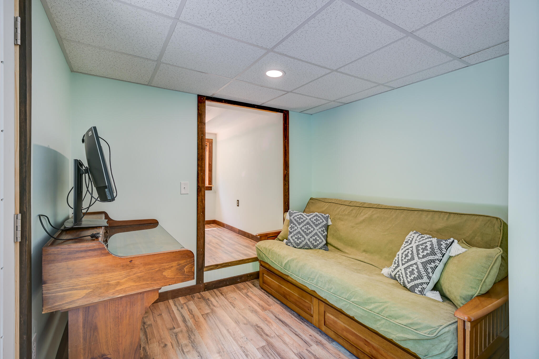 Finished basement sitting room with a green sofa and built-in wooden desk.