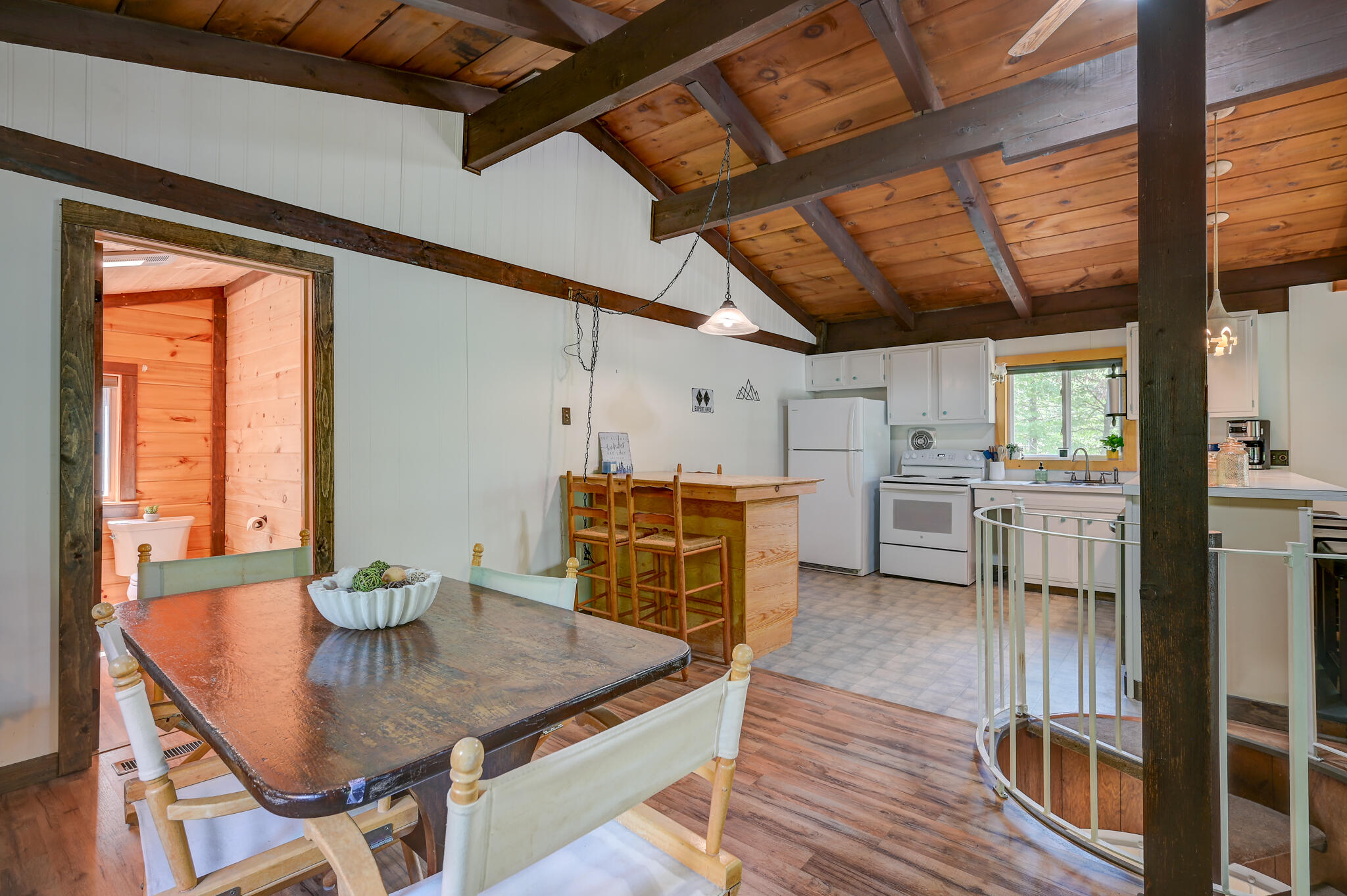 Open dining and kitchen area with a vaulted wood-beam ceiling, central island, and spiral staircase.
